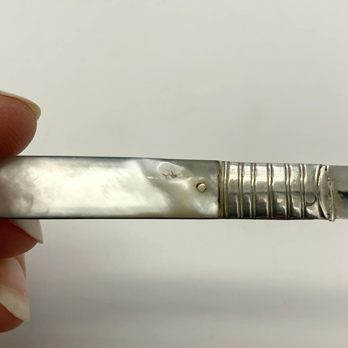A close-up of a small chip on a mother of pearl handle, held at the left edge by fingers against a plain light background.