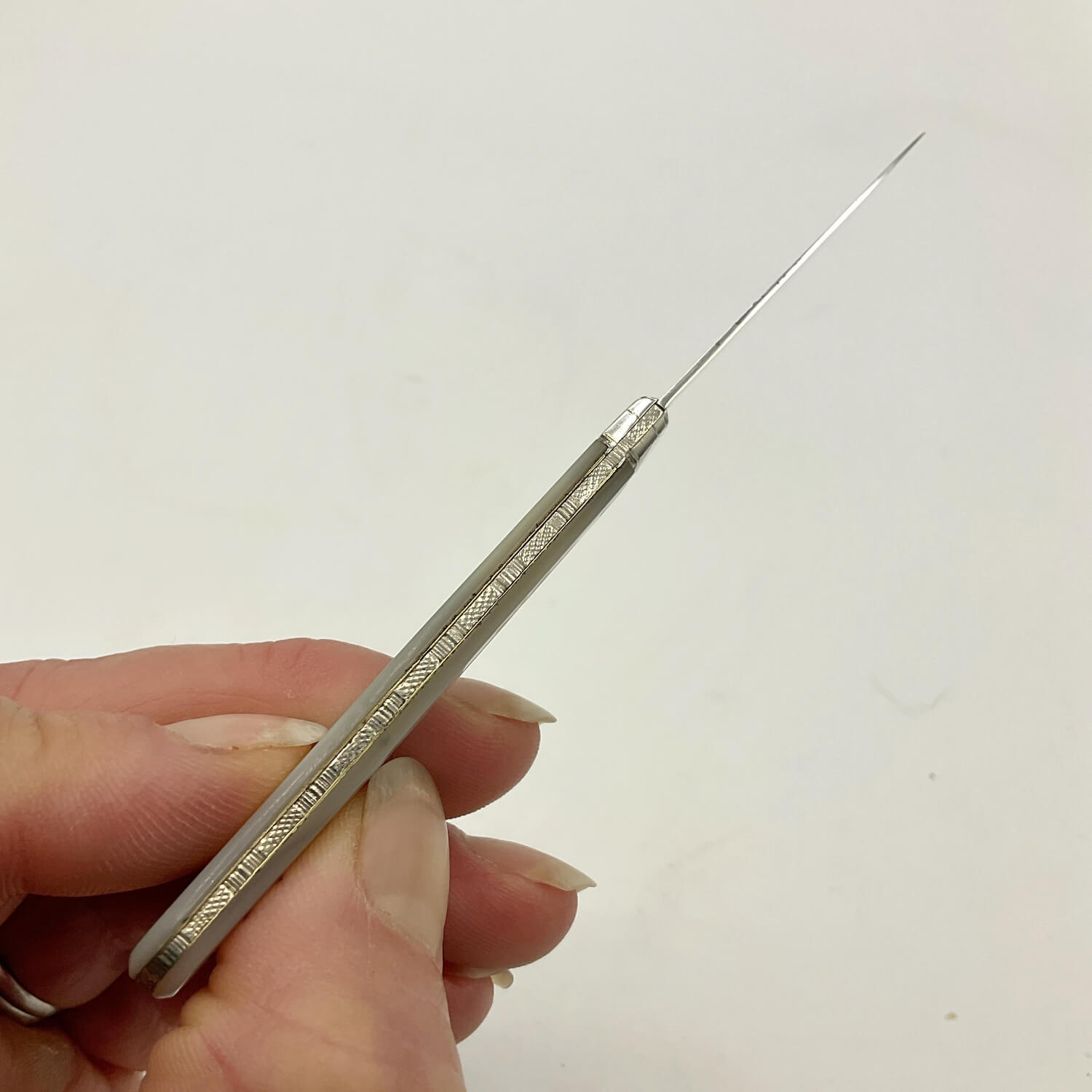 A hand holding a silver fruit knife with a long, slender shaft and a textured handle, shown against a plain off-white background.
