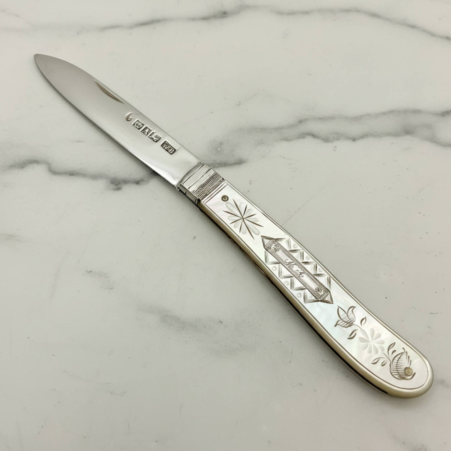 A antique silver fruit knife with an engraved mother-of-pearl handle, shown diagonally on a light gray background.