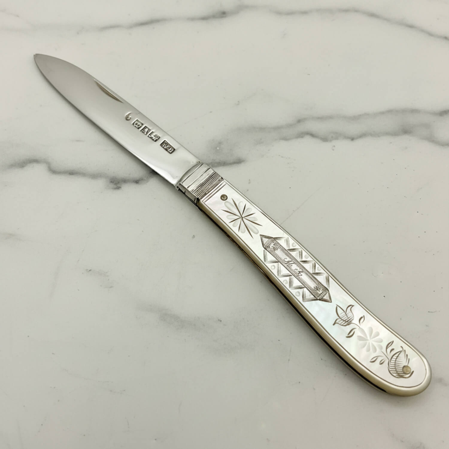 A antique silver fruit knife with an engraved mother-of-pearl handle, shown diagonally on a light gray background.
