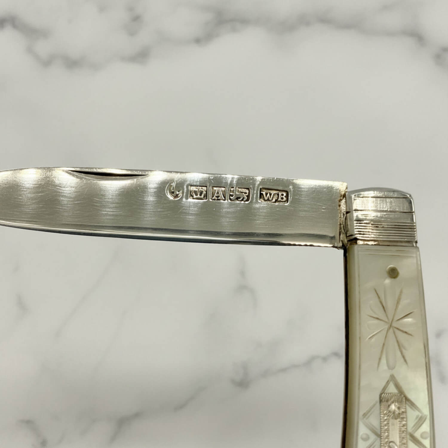 Close-up of a folding pocket knife with a silver blade and a white mother-of-pearl handle featuring engraved star and geometric patterns.