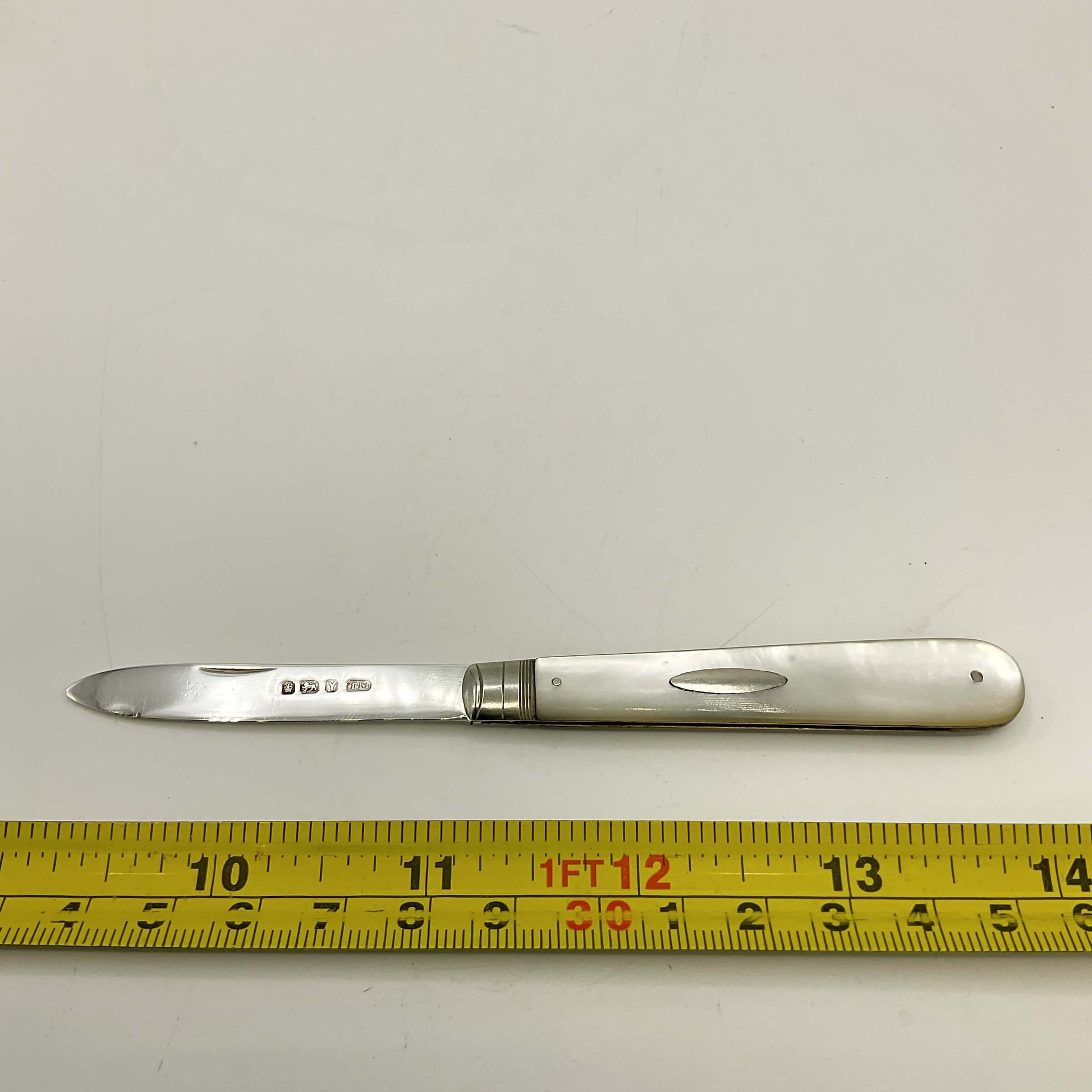 Silver fruit knife with a measuring tape for scale on a white background