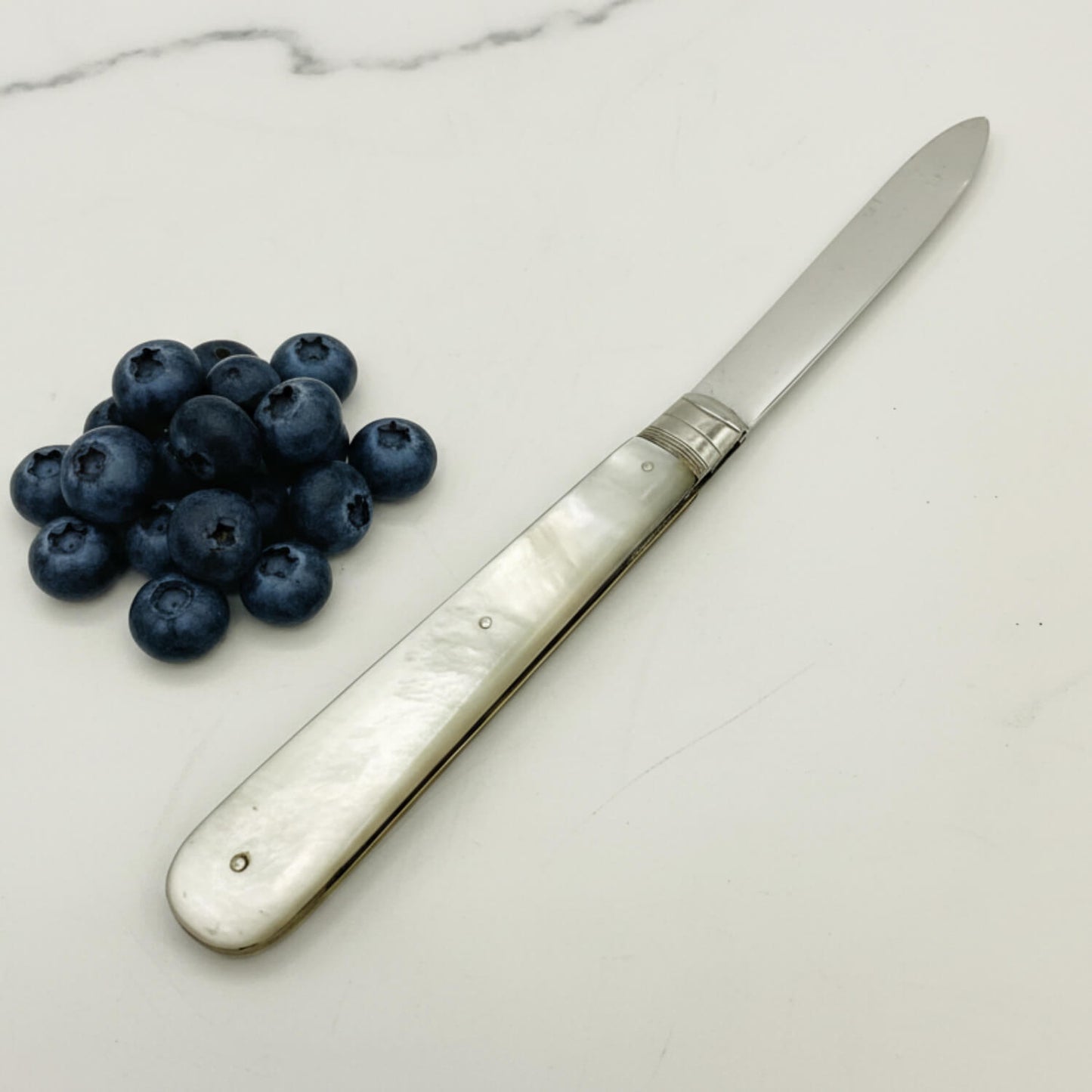 Silver knife with a decorative handle next to blueberries on a marble surface