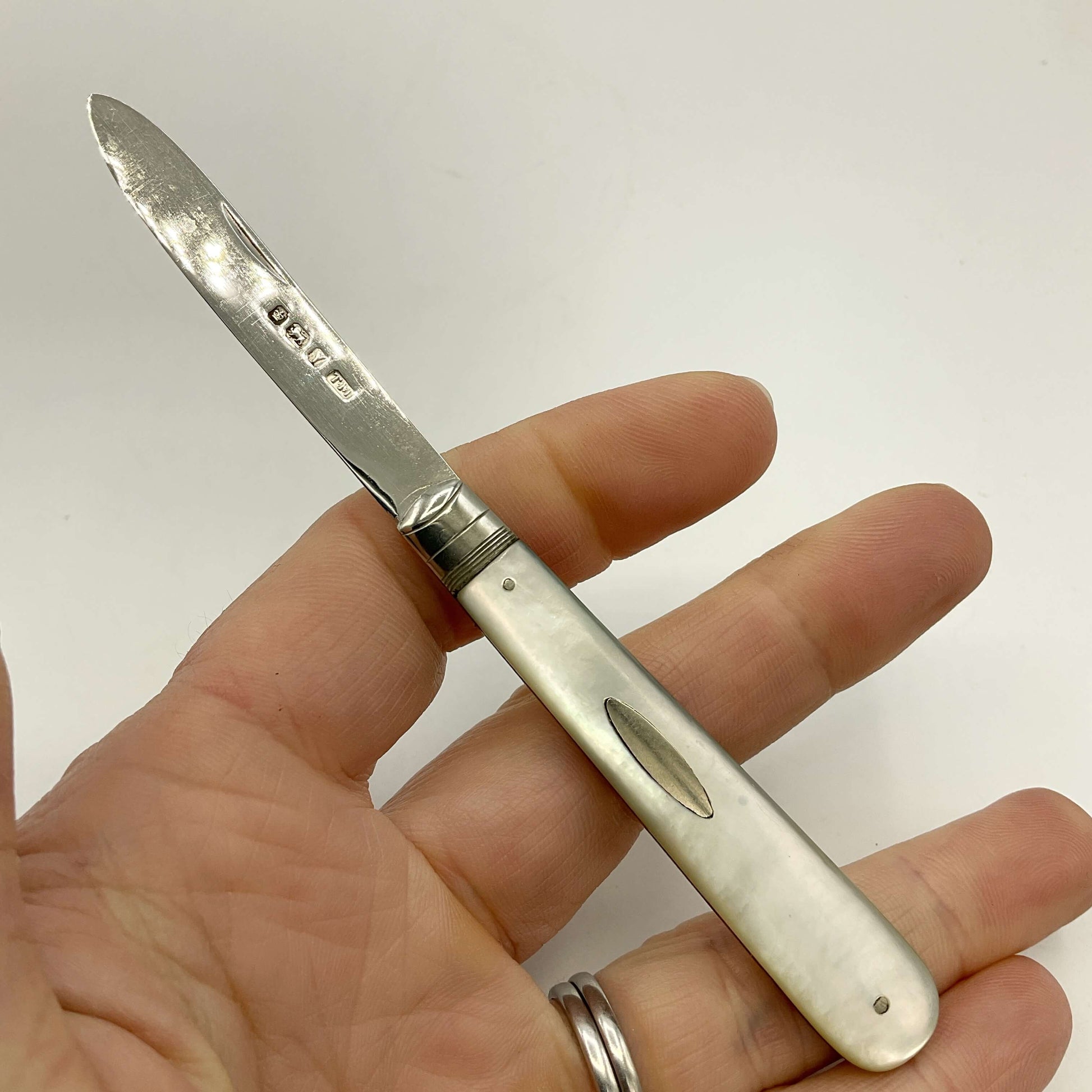 Silver fruit knife held in a hand against a white background