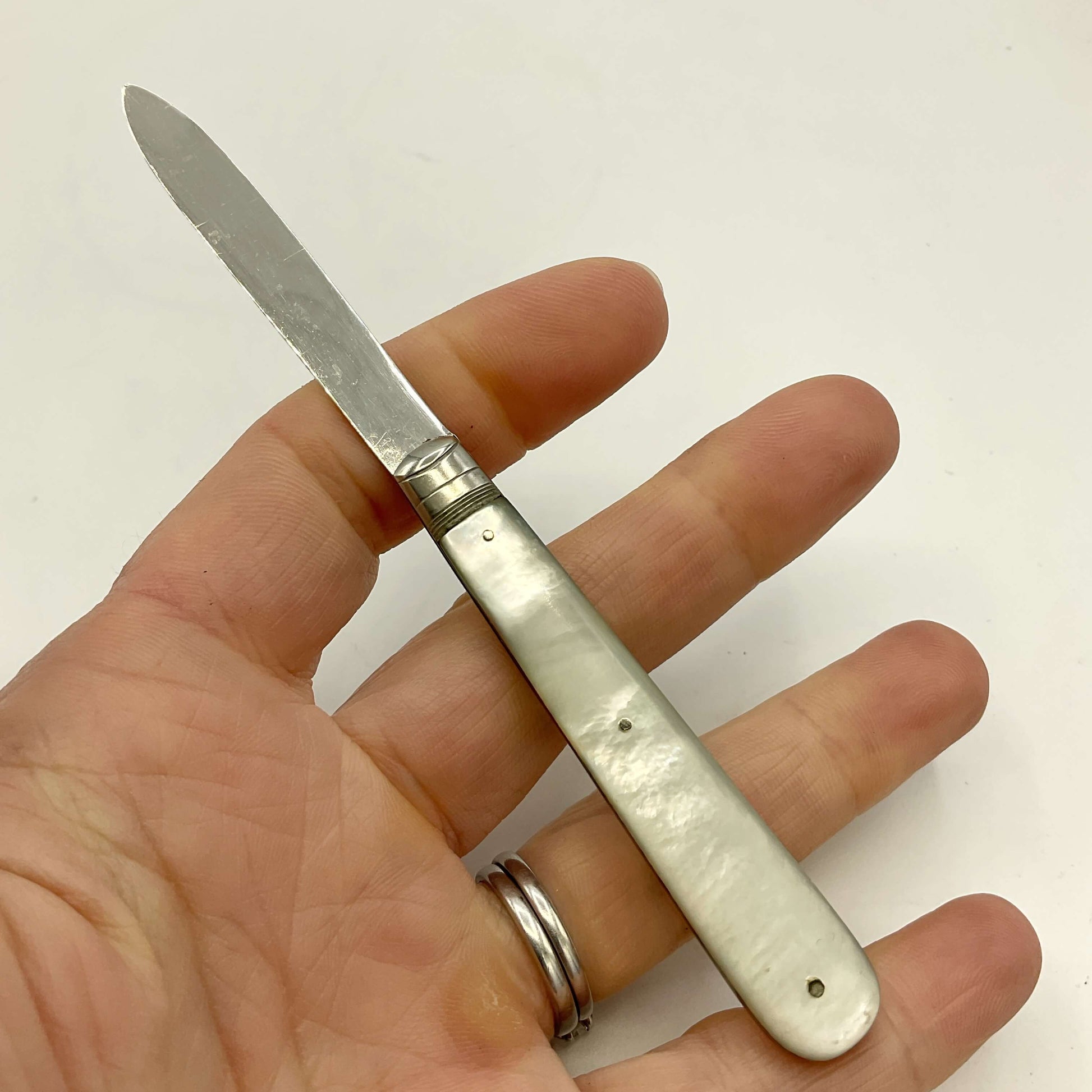 Hand holding a small fruit knife with a silver blade and pearl handle against a white background