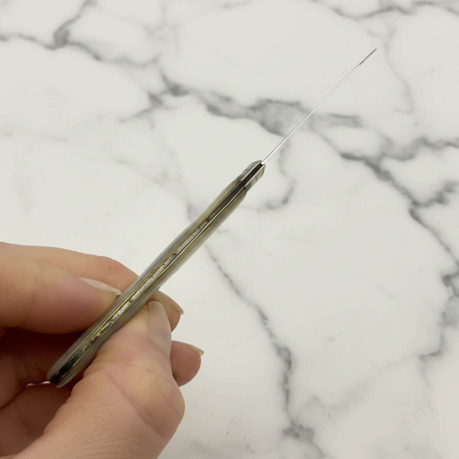 Hand holding a fruit knife showing the top if it against a marble background
