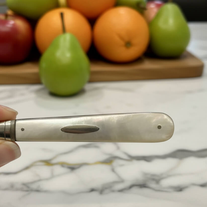 fruit knife pearl handle held in hand with fruits in the background