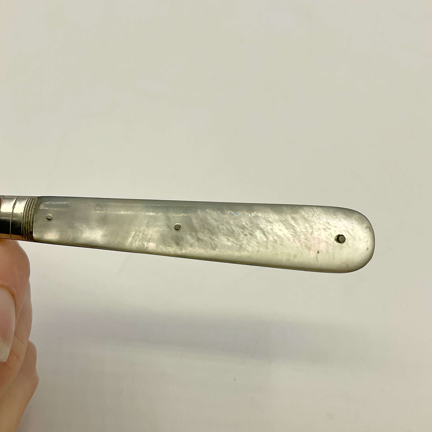 mother of pearl fruit knife handle by a hand against a plain background