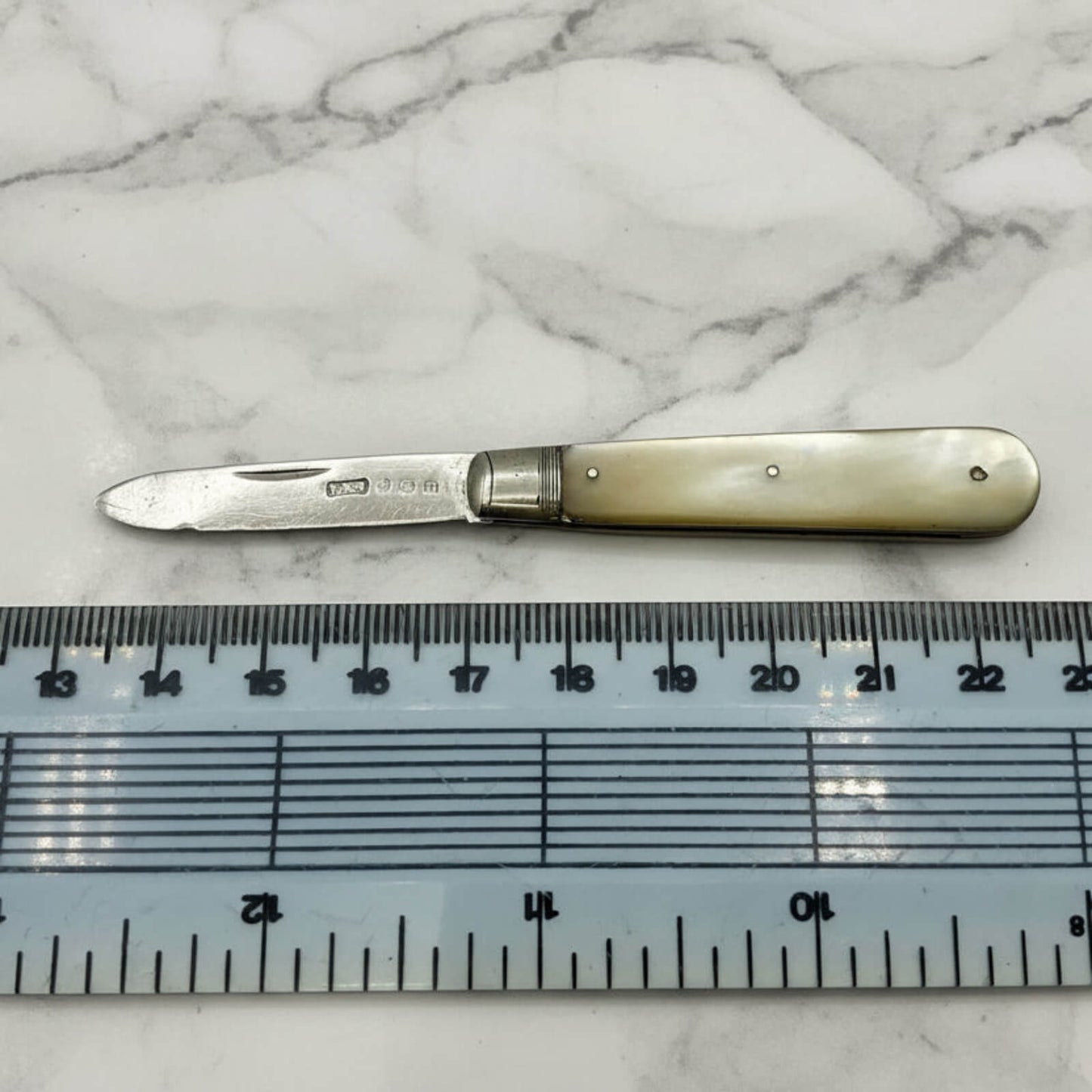 Foldable knife with a decorative handle on a marble surface next to a ruler for scale.