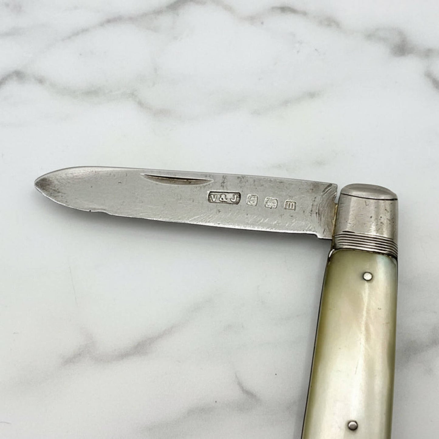 Vintage folding knife with a silver blade and pearl handle on a marble surface