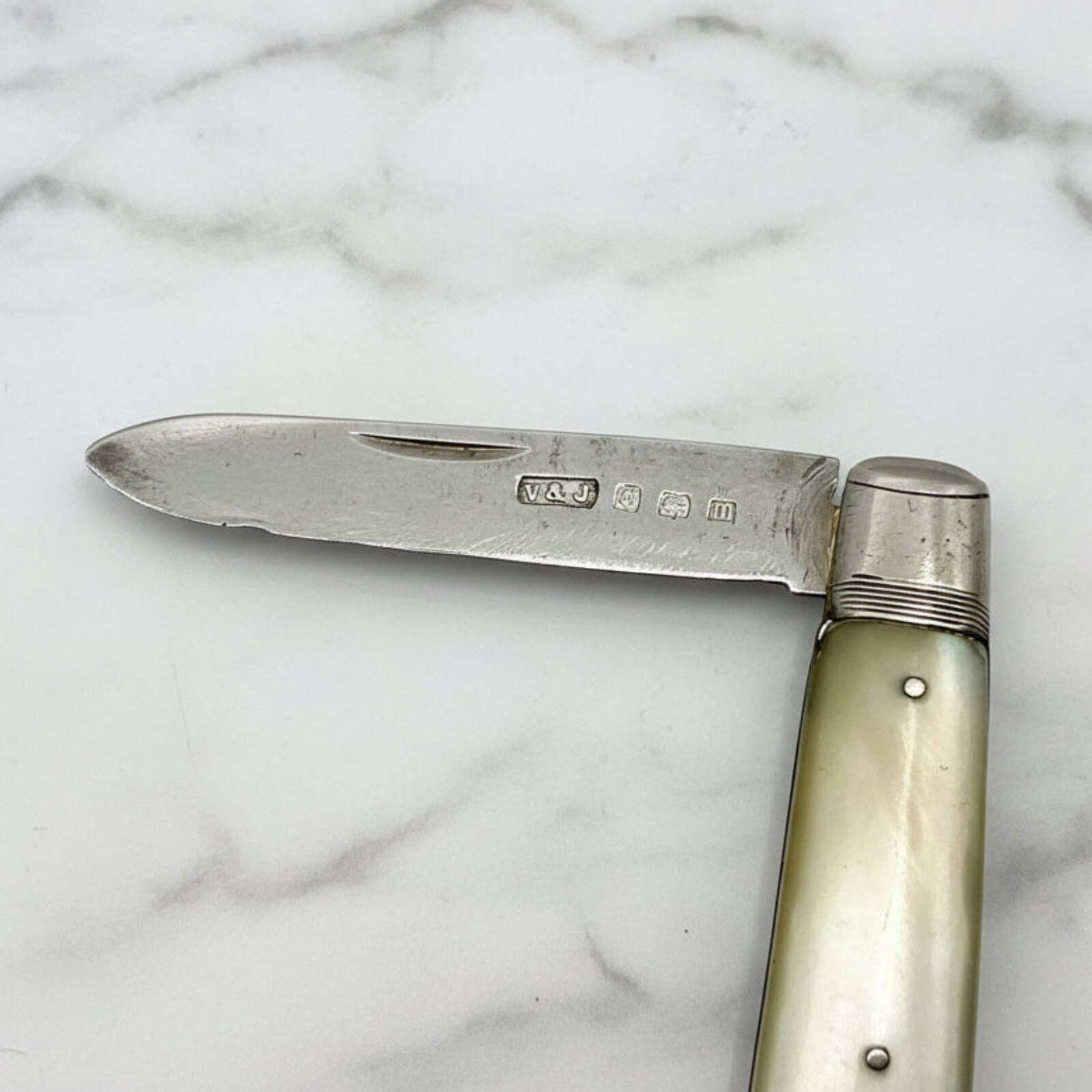 Vintage folding knife with a silver blade and pearl handle on a marble surface