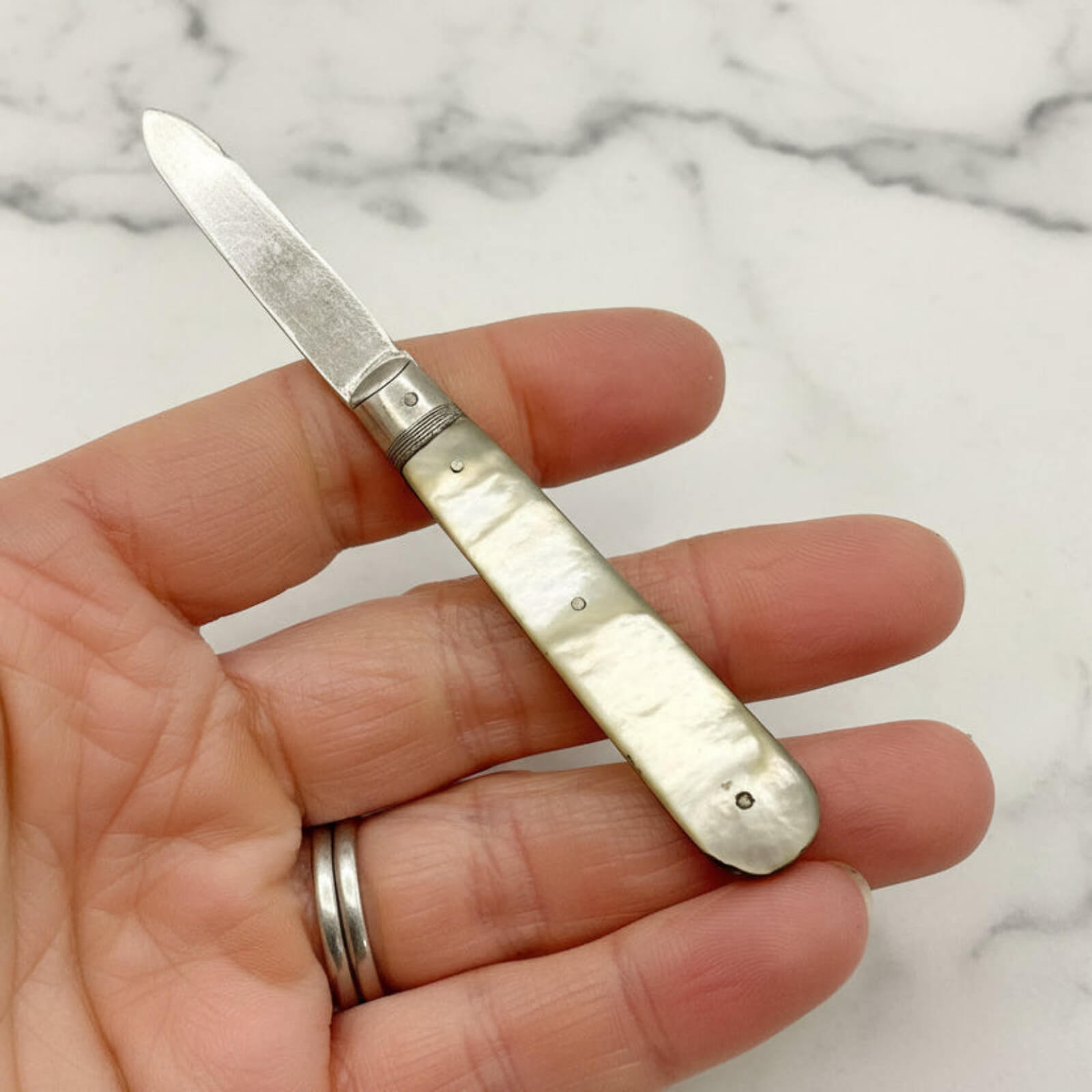 Hand holding a small folding knife with a decorative handle on a marble background