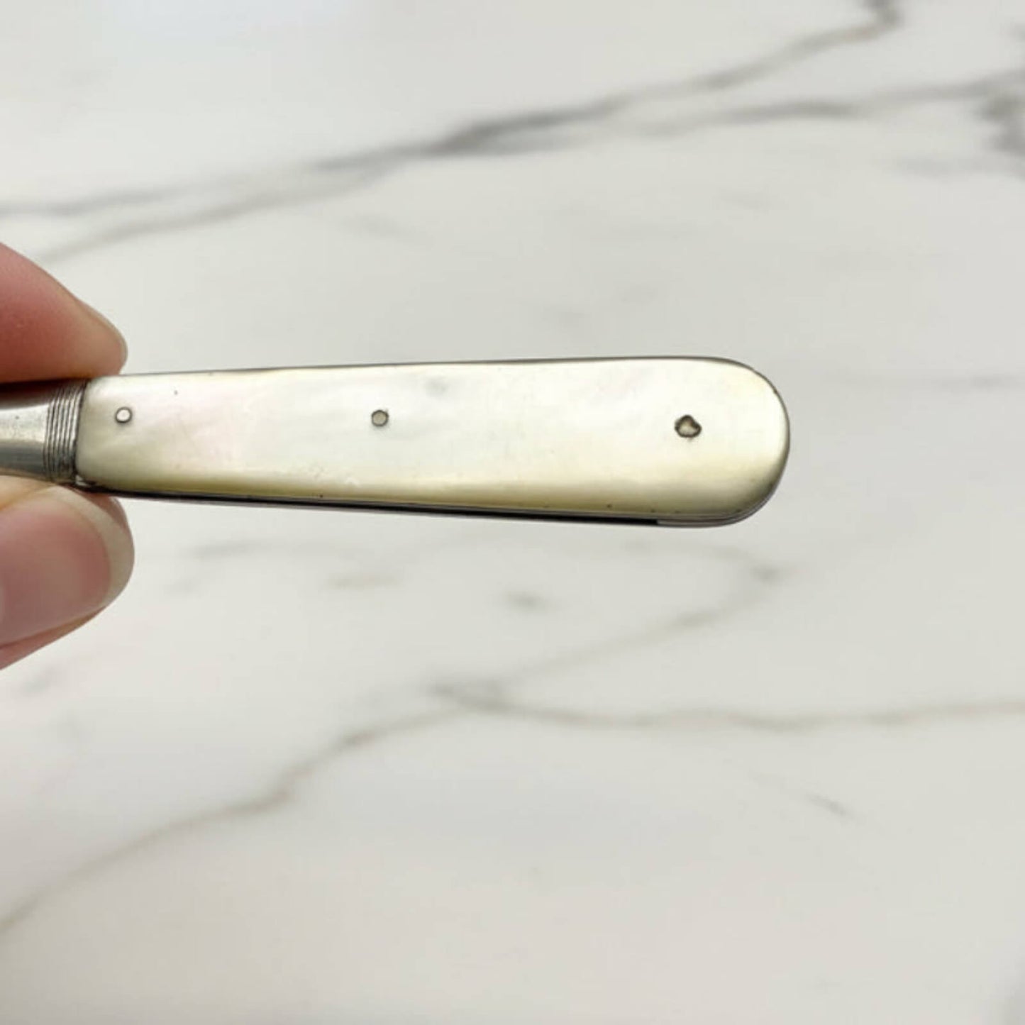 fruit knife handle held by a hand against a marble background