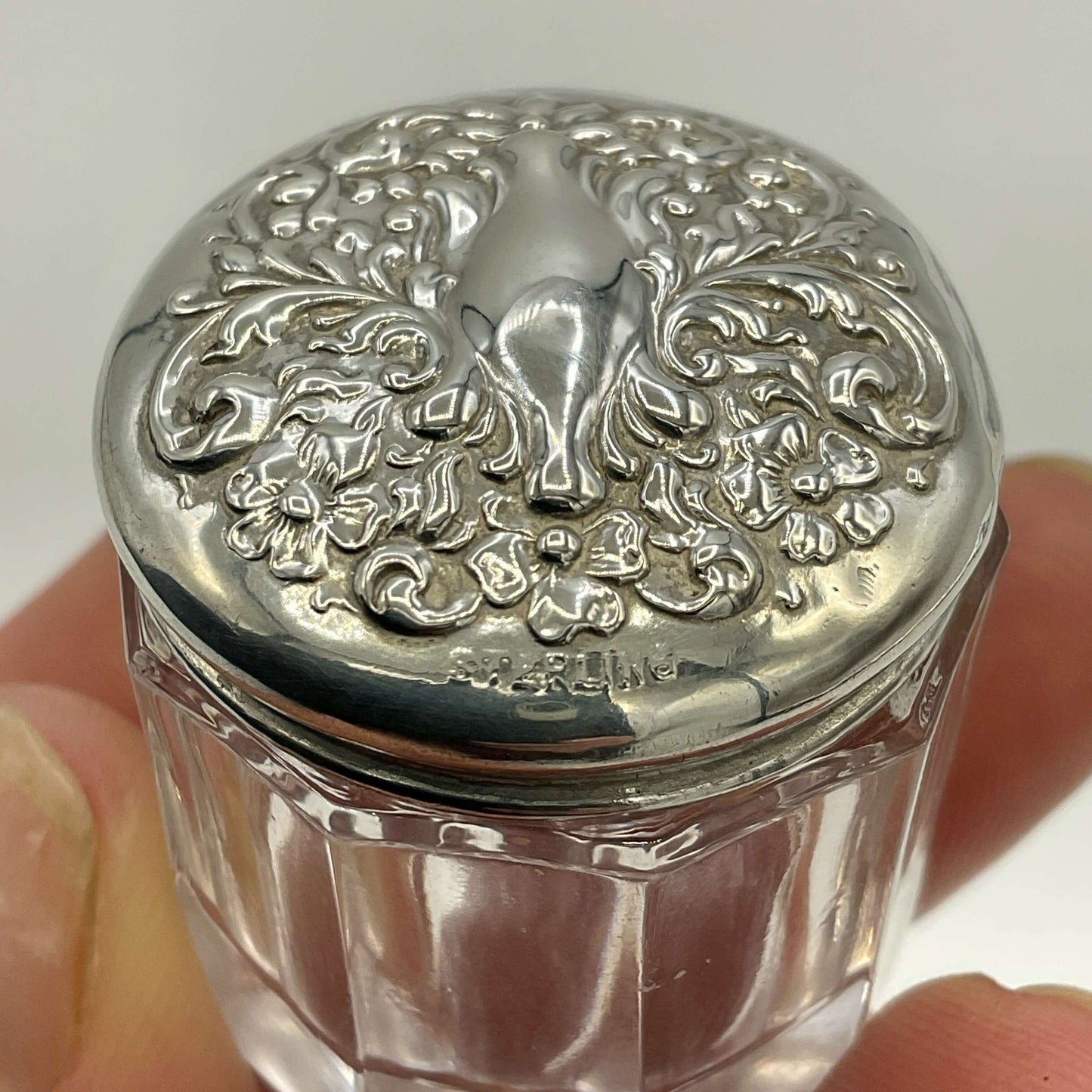 Decorative glass jar with a silver lid featuring intricate patterns.