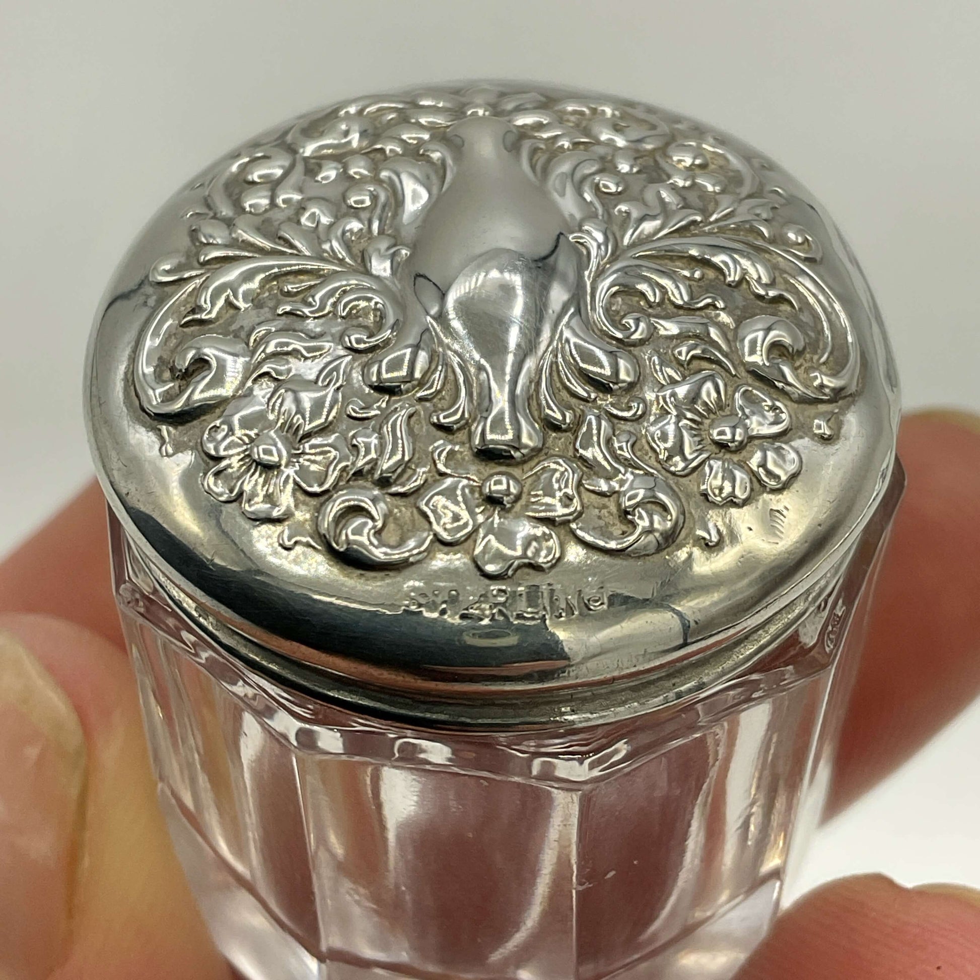 Decorative glass jar with a silver lid featuring intricate patterns.