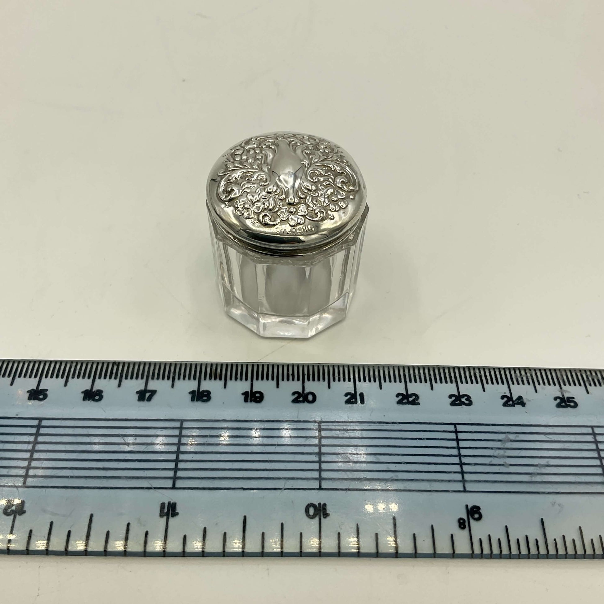 Small glass jar with silver lid on a white background with a ruler for scale.