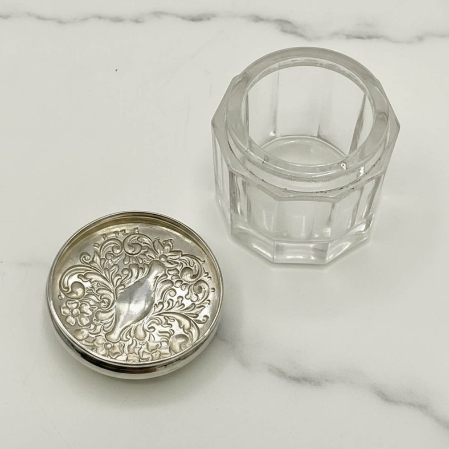 Inside of Decorative silver lid and clear glass container on a marble surface