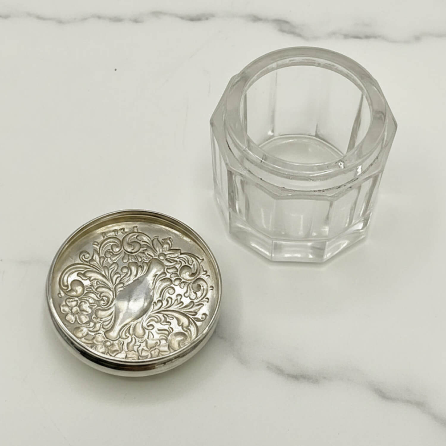 Inside of Decorative silver lid and clear glass container on a marble surface