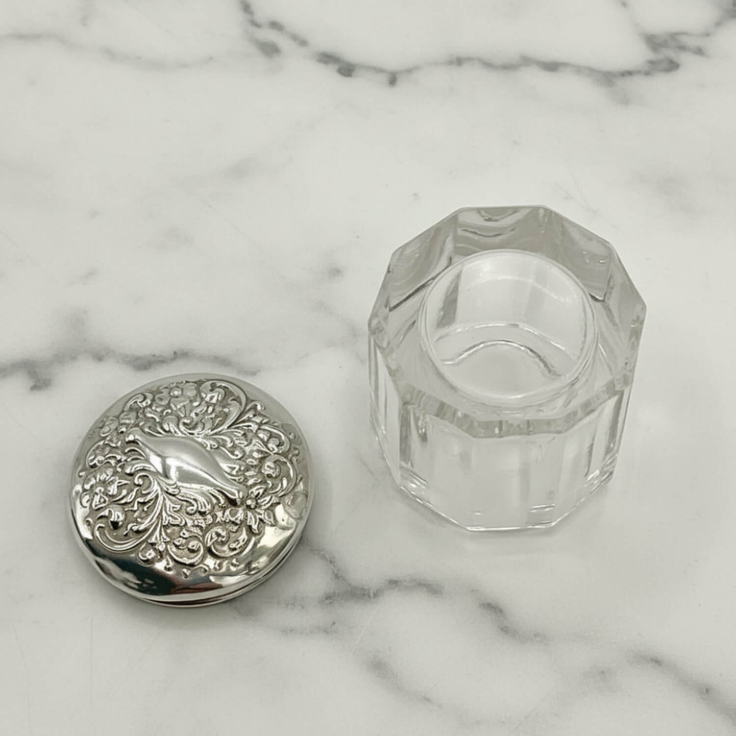 Silver decorative lid and clear glass container on a marble surface
