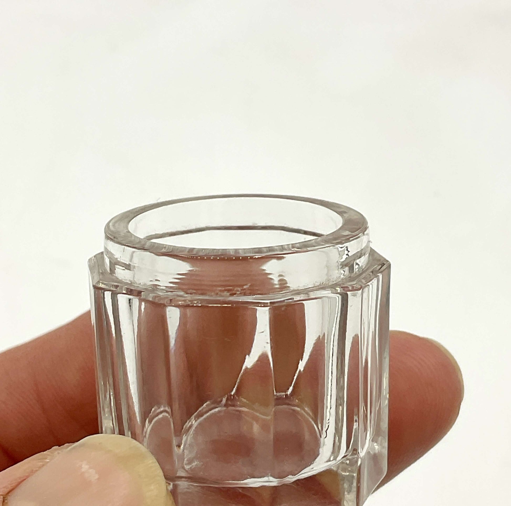 Clear glass hexagonal jar held between fingers against a white background