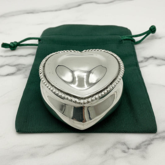 Silver heart-shaped trinket box on a green drawstring bag with a marble background