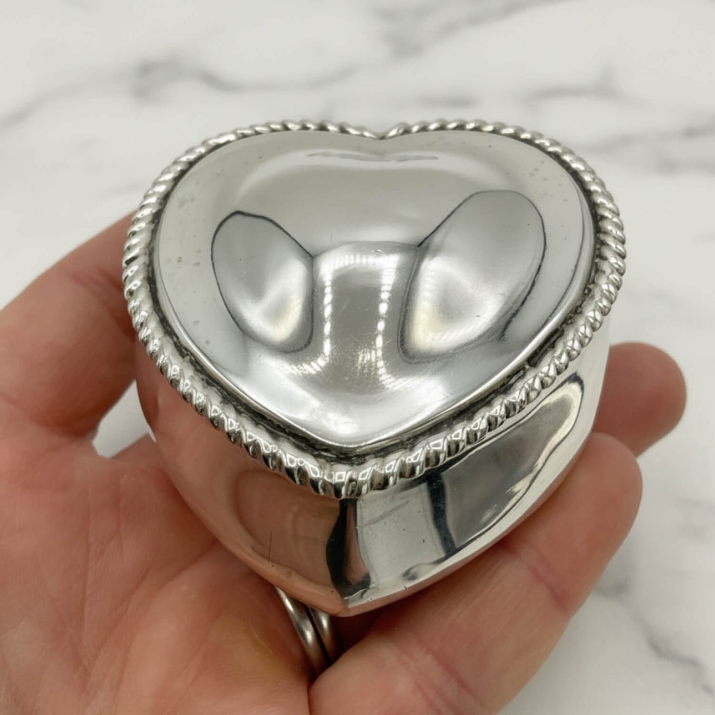Heart-shaped silver box held in a hand with a marble background