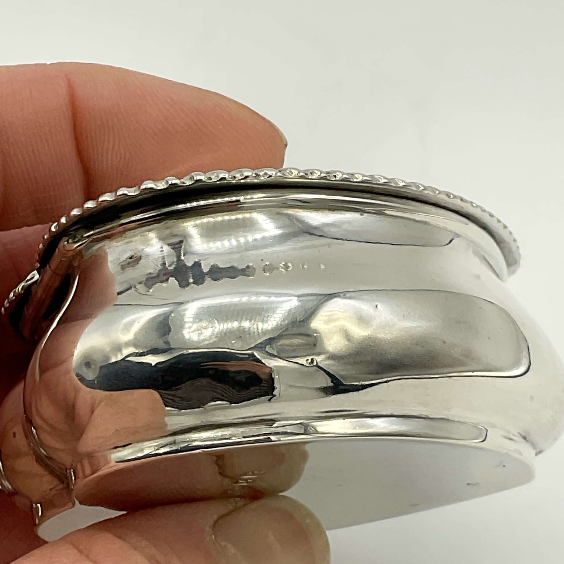 Close-up of a silver box with intricate design held by a hand against a white background