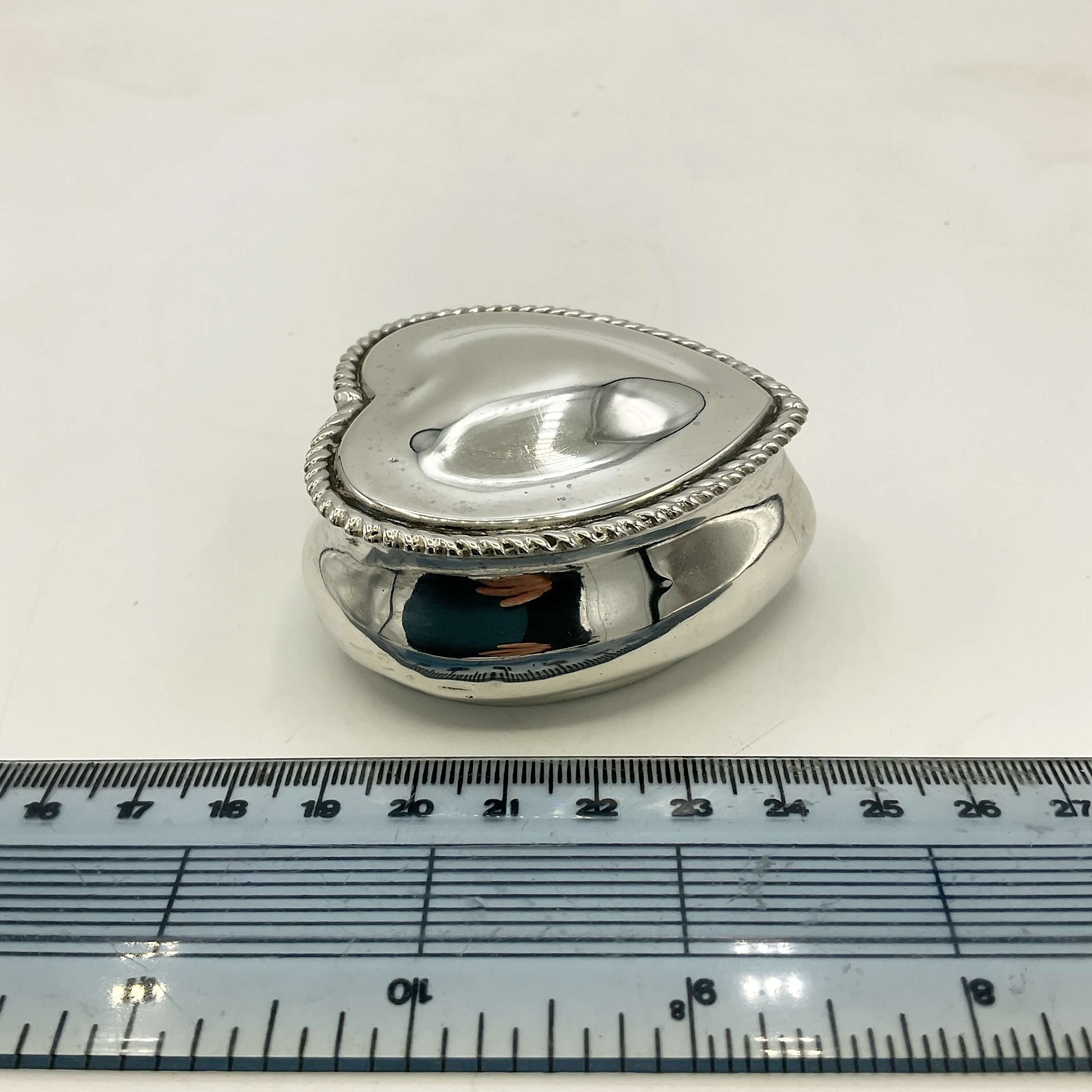 Silver heart-shaped box with a ruler for scale on a white background
