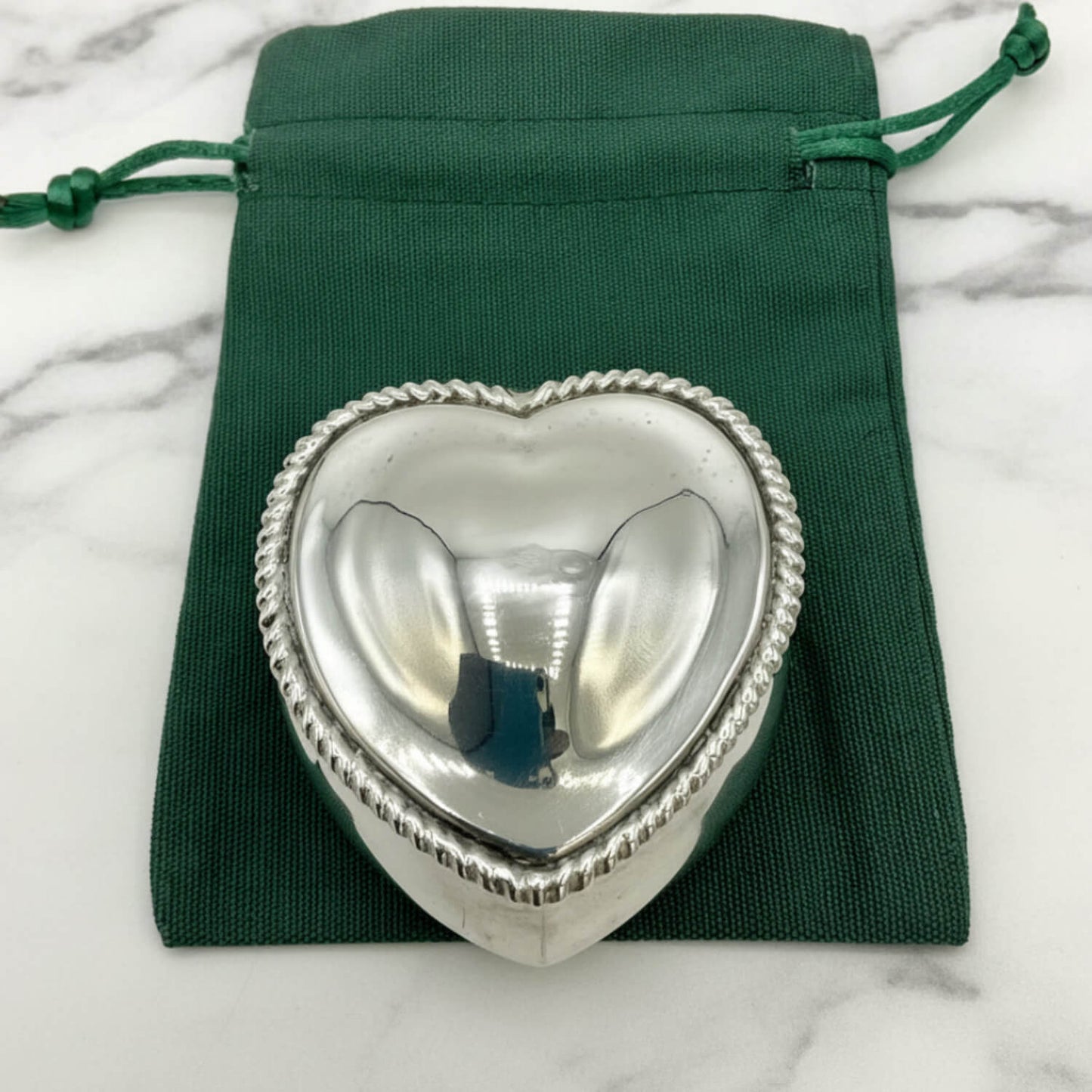 Silver heart-shaped box on a green drawstring bag with marble background
