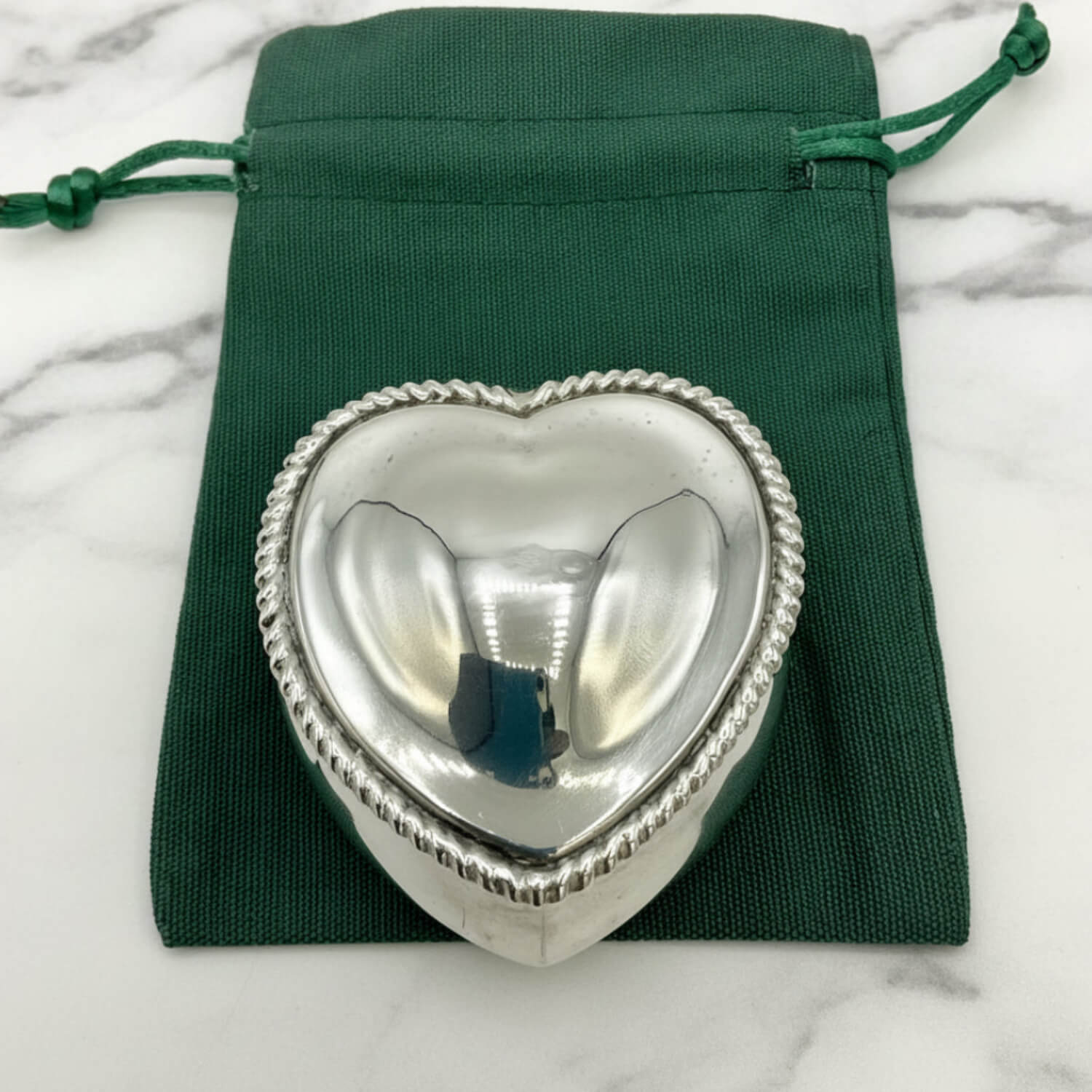 Silver heart-shaped box on a green drawstring bag with marble background