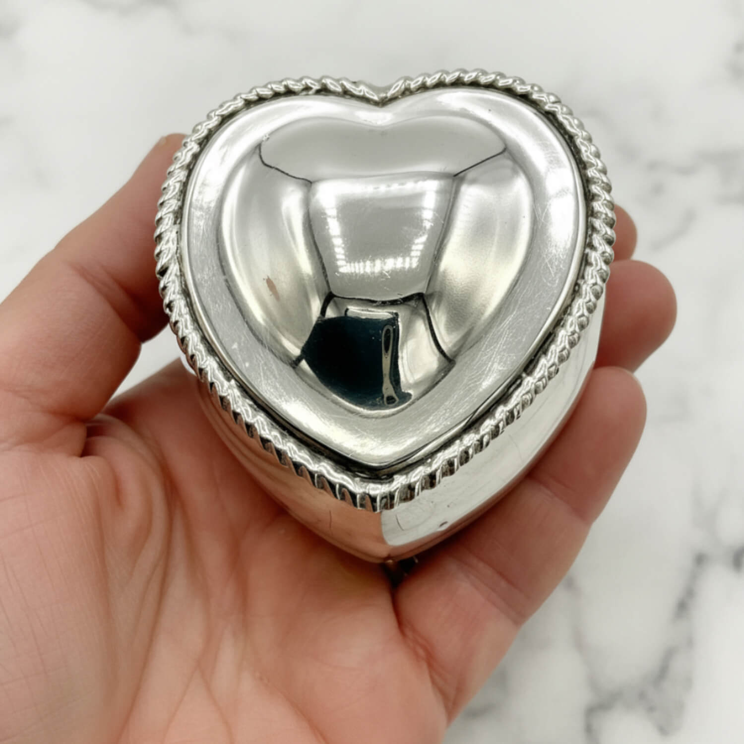 Silver heart-shaped box held in a hand against a marble background