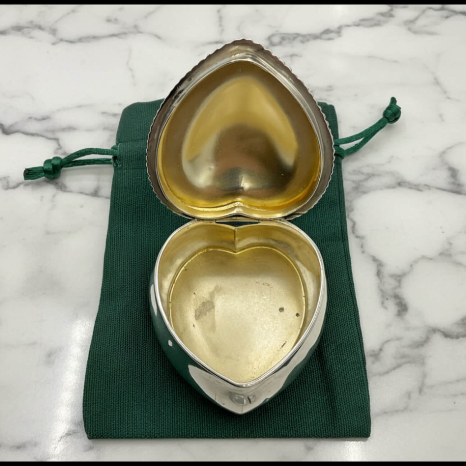inside of Antique Sterling Silver Heart Shaped Jewellery Box on a green bag and maeble worktop