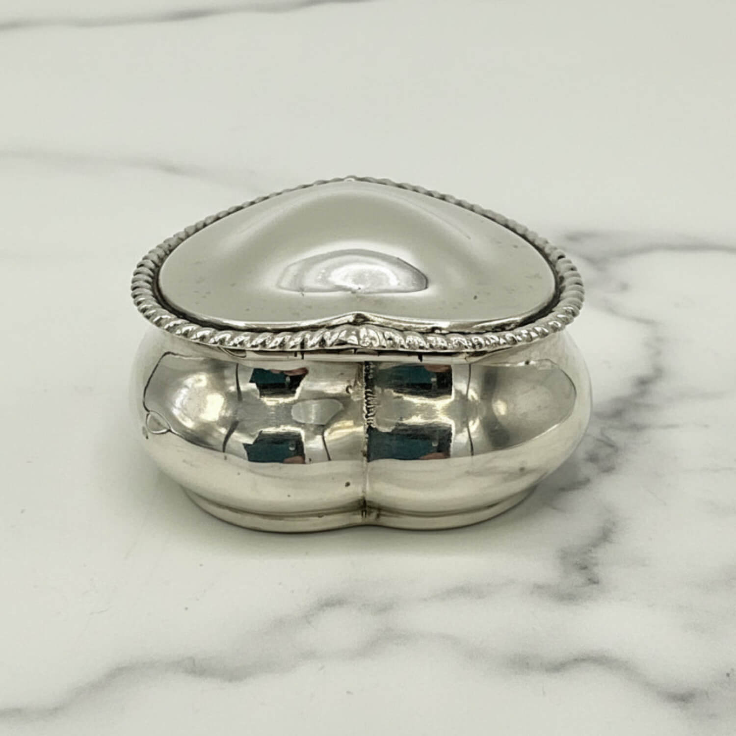 Silver heart-shaped jewelry box on a marble surface