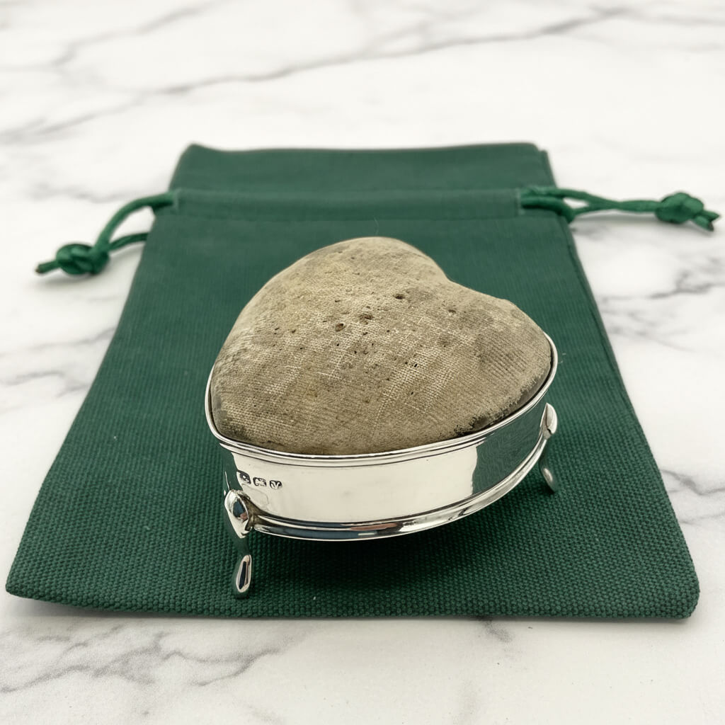 Heart-shaped pincushion with silver base on a green drawstring bag