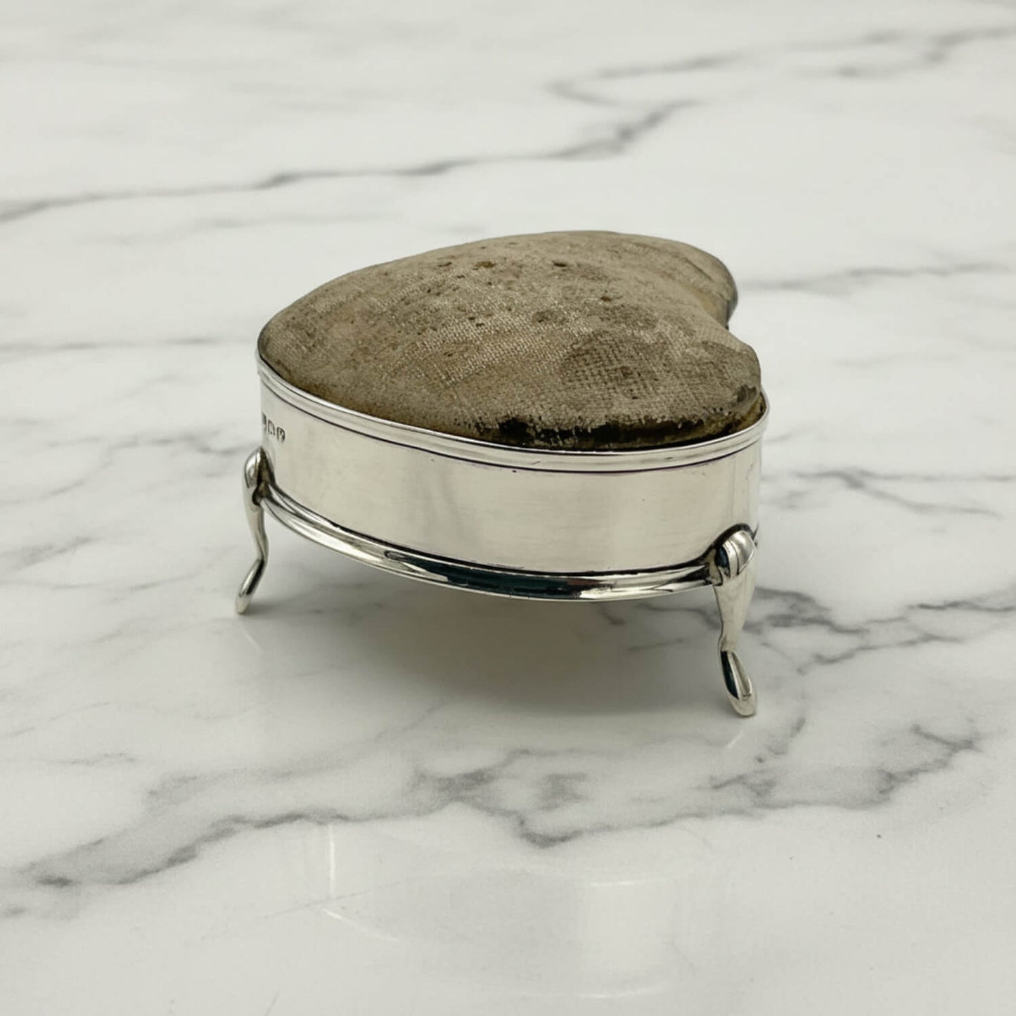 Silver pincushion with a textured lid on a marble surface