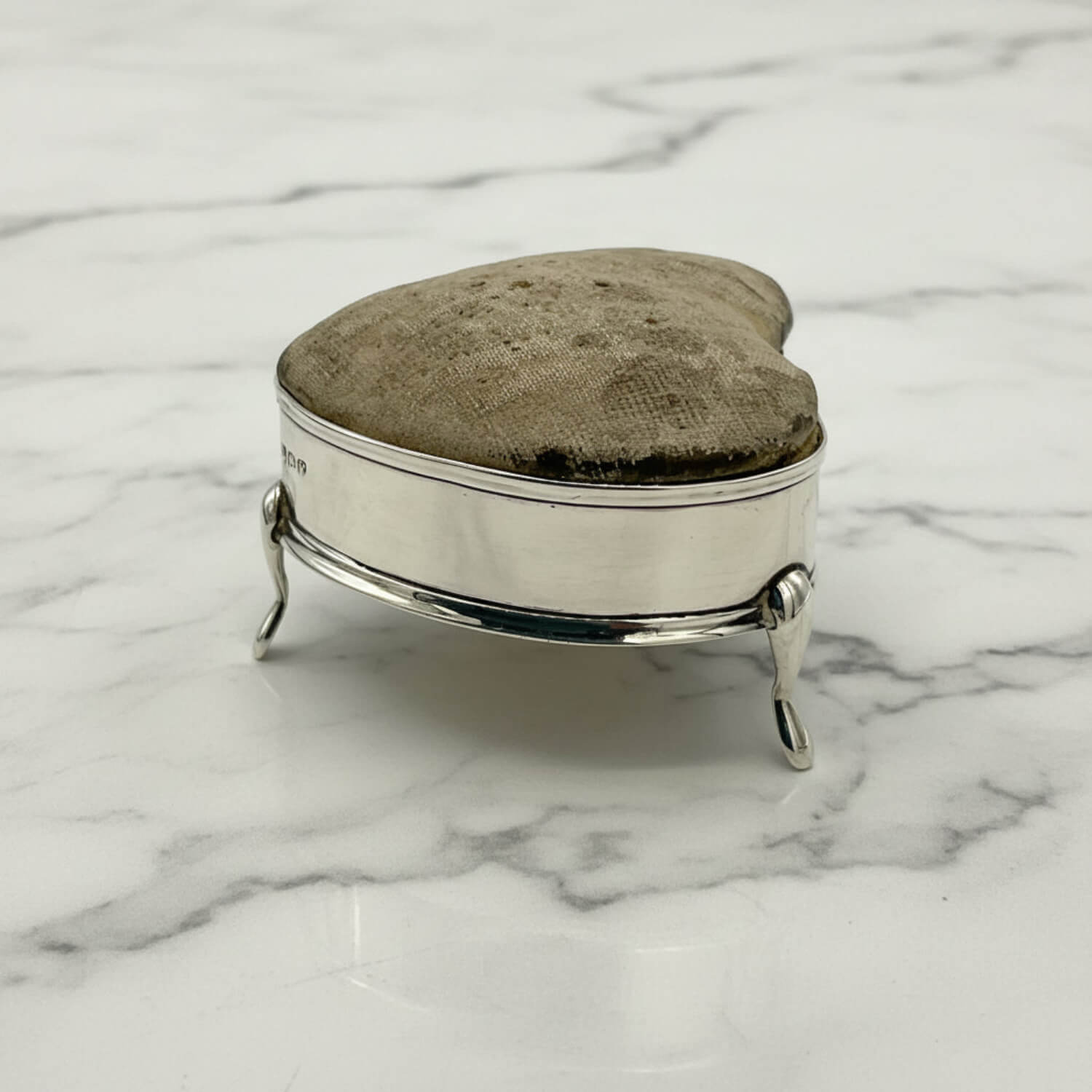 Silver pincushion with a textured lid on a marble surface