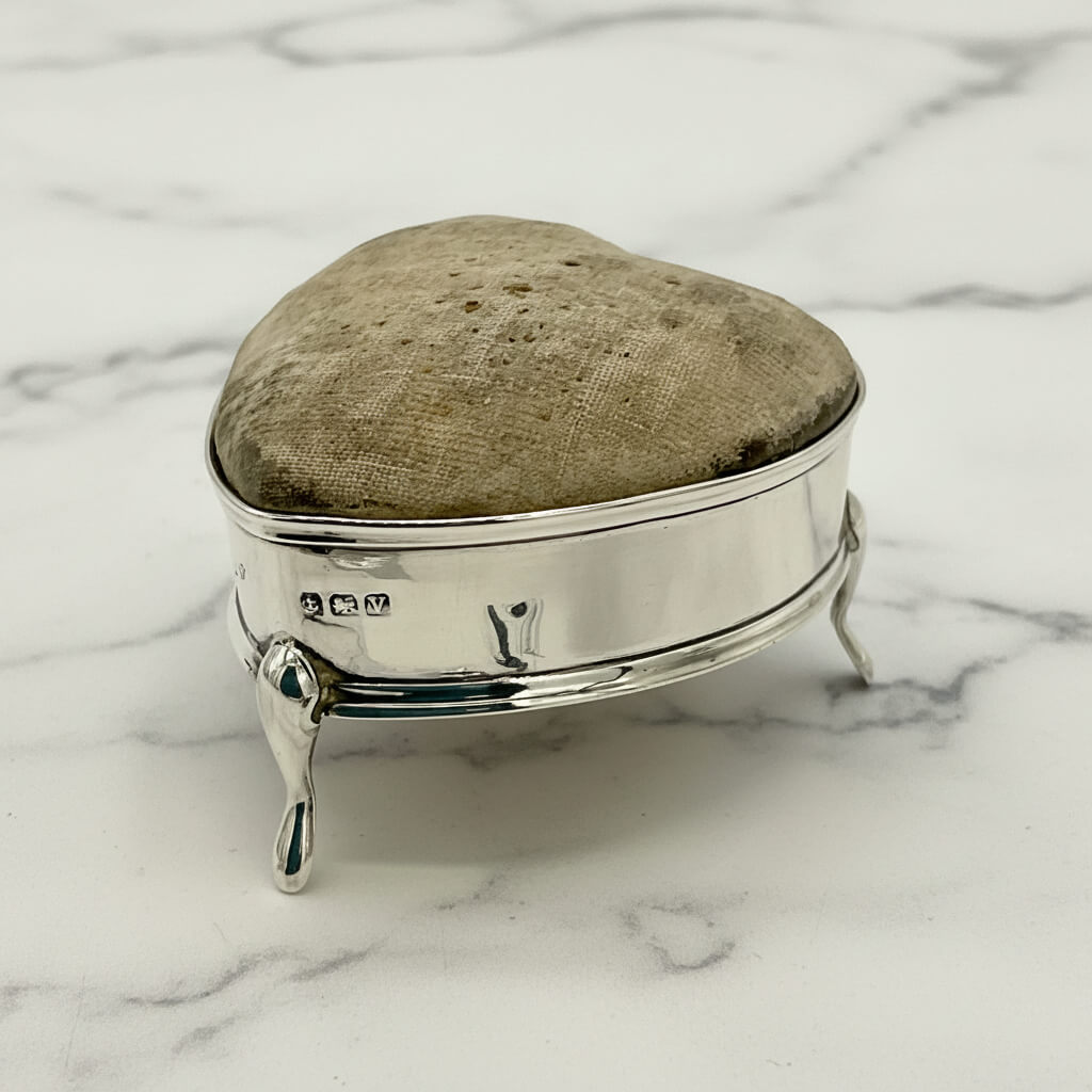 Silver pincushion with hallmarks and a textured lid on a marble surface