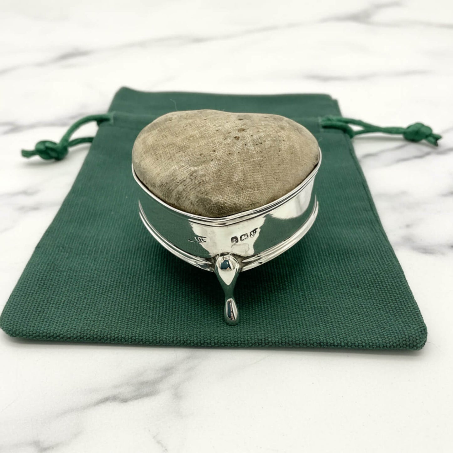 Silver pincushion on a green fabric pouch against a marble background