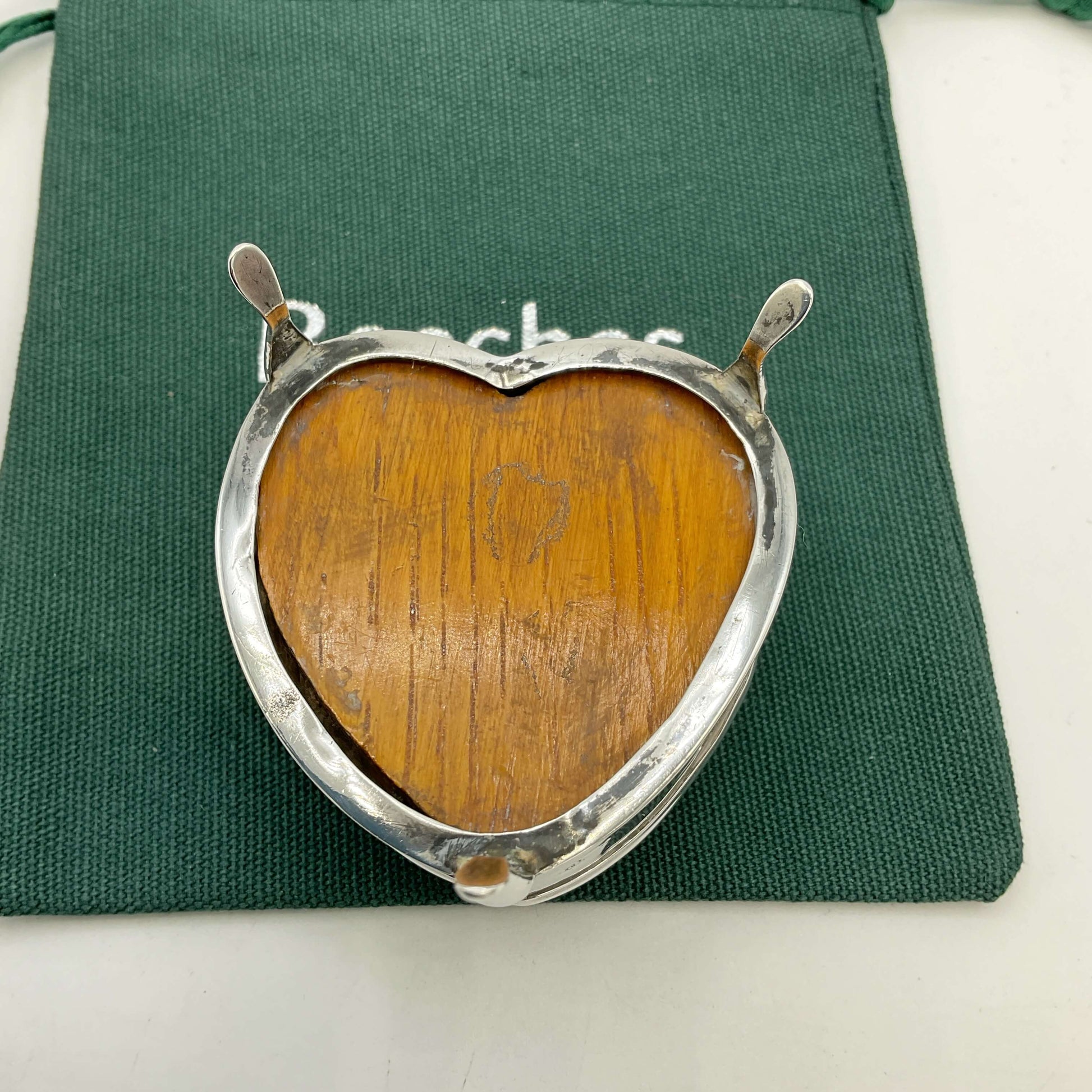 Heart-shaped pincushion with wooden base and silver frame on a green fabric background