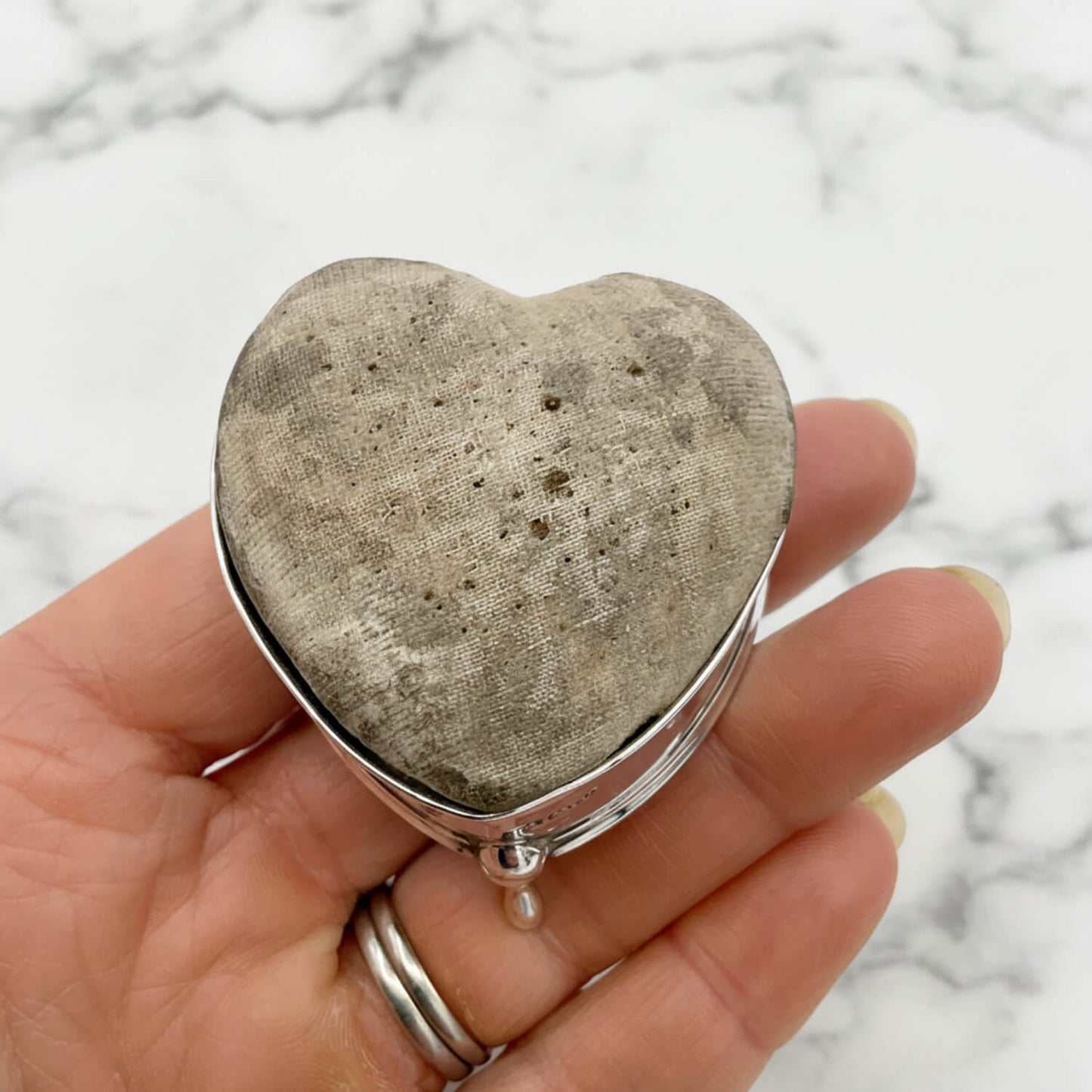Heart-shaped pincushion held in a hand with a marble background