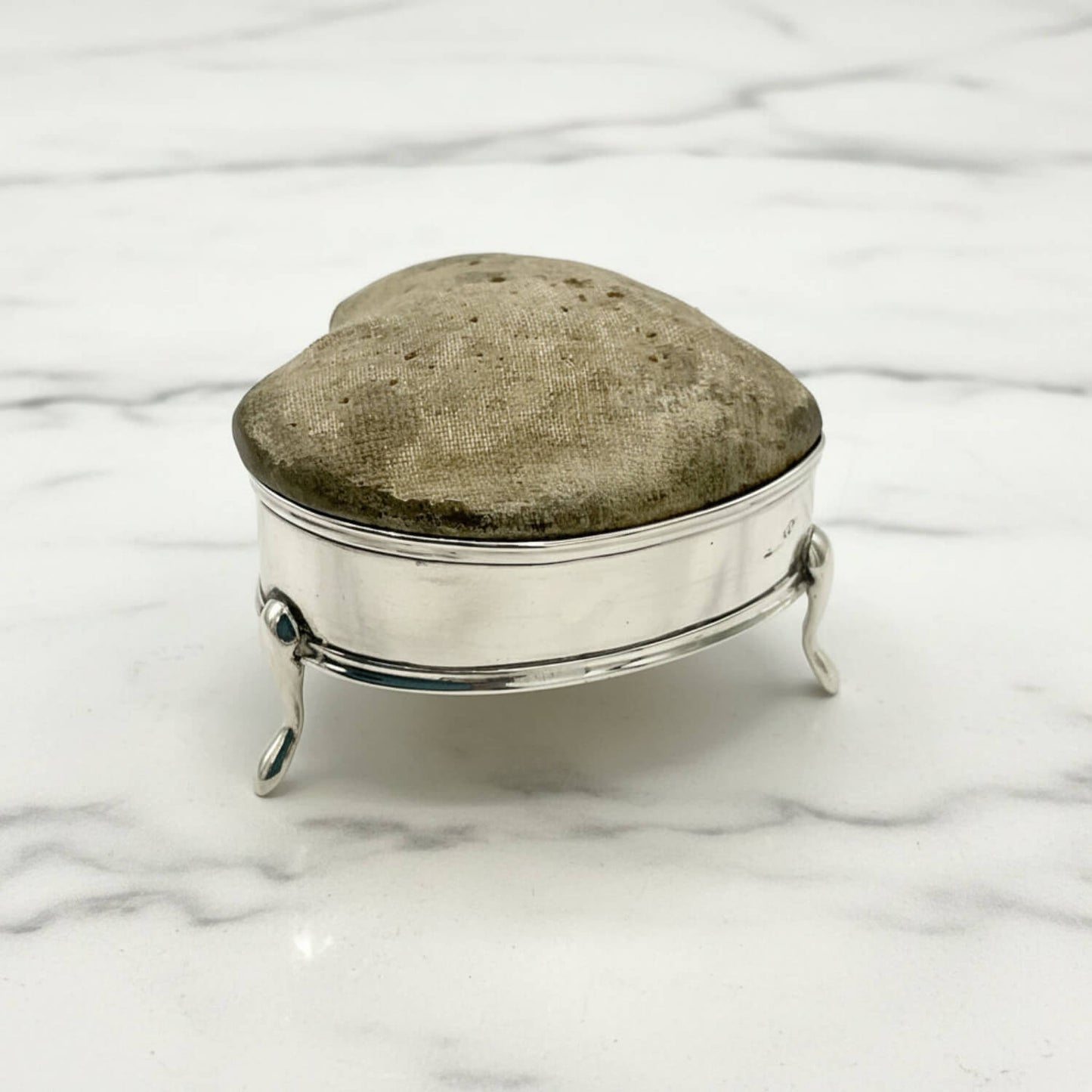 Silver pincushion with a textured top on a marble surface