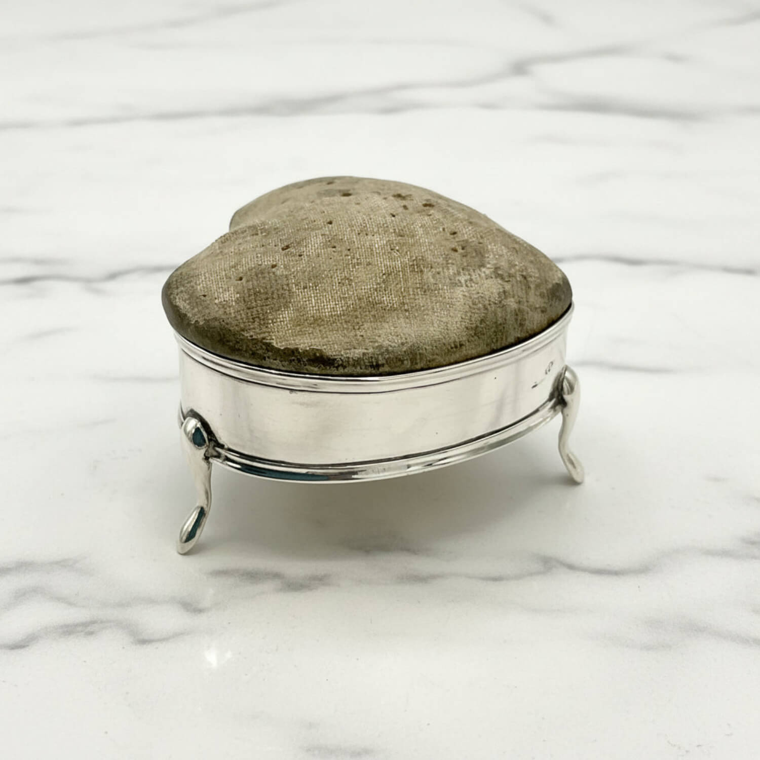 Silver pincushion with a textured top on a marble surface