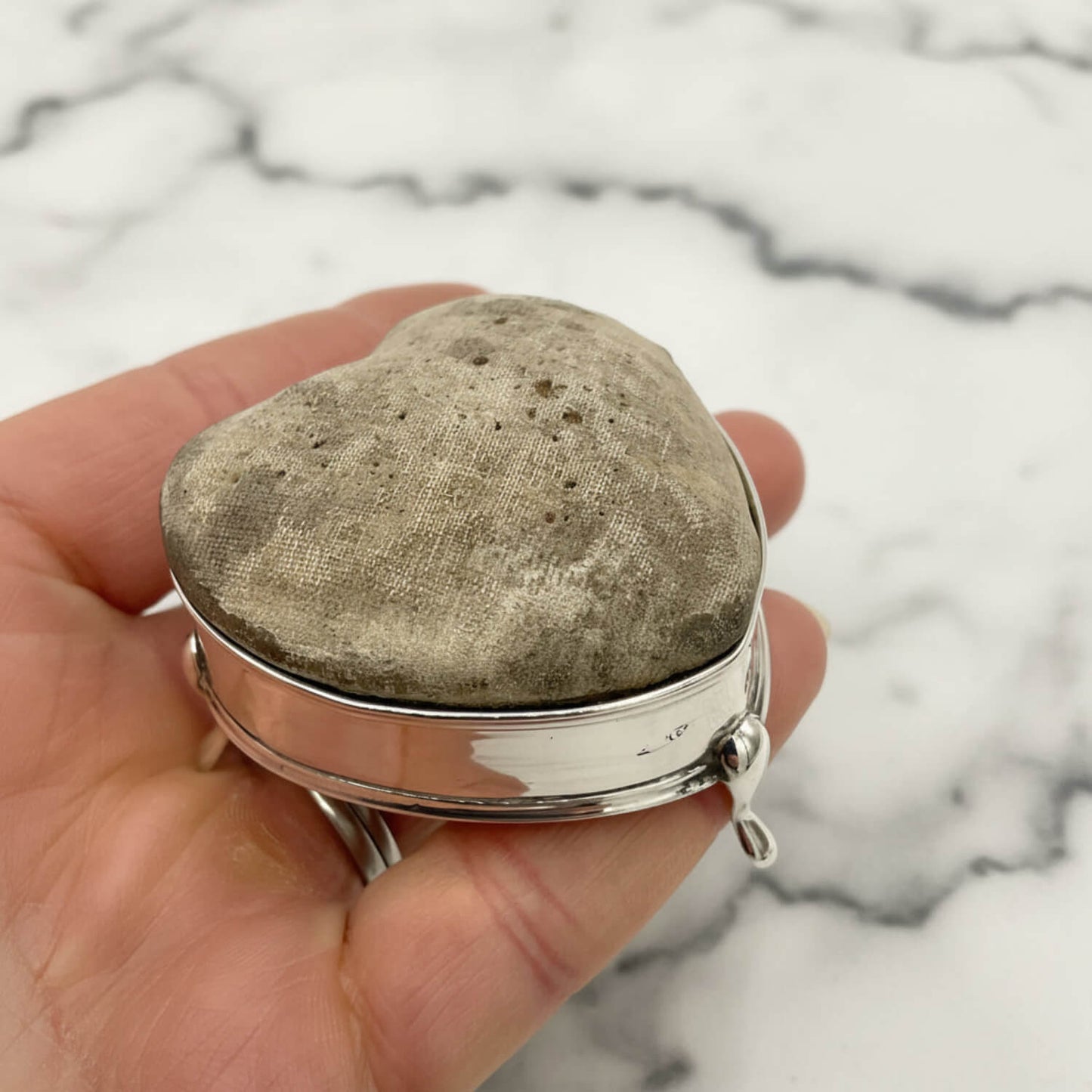 Heart-shaped pincushion held in a hand with a marble background