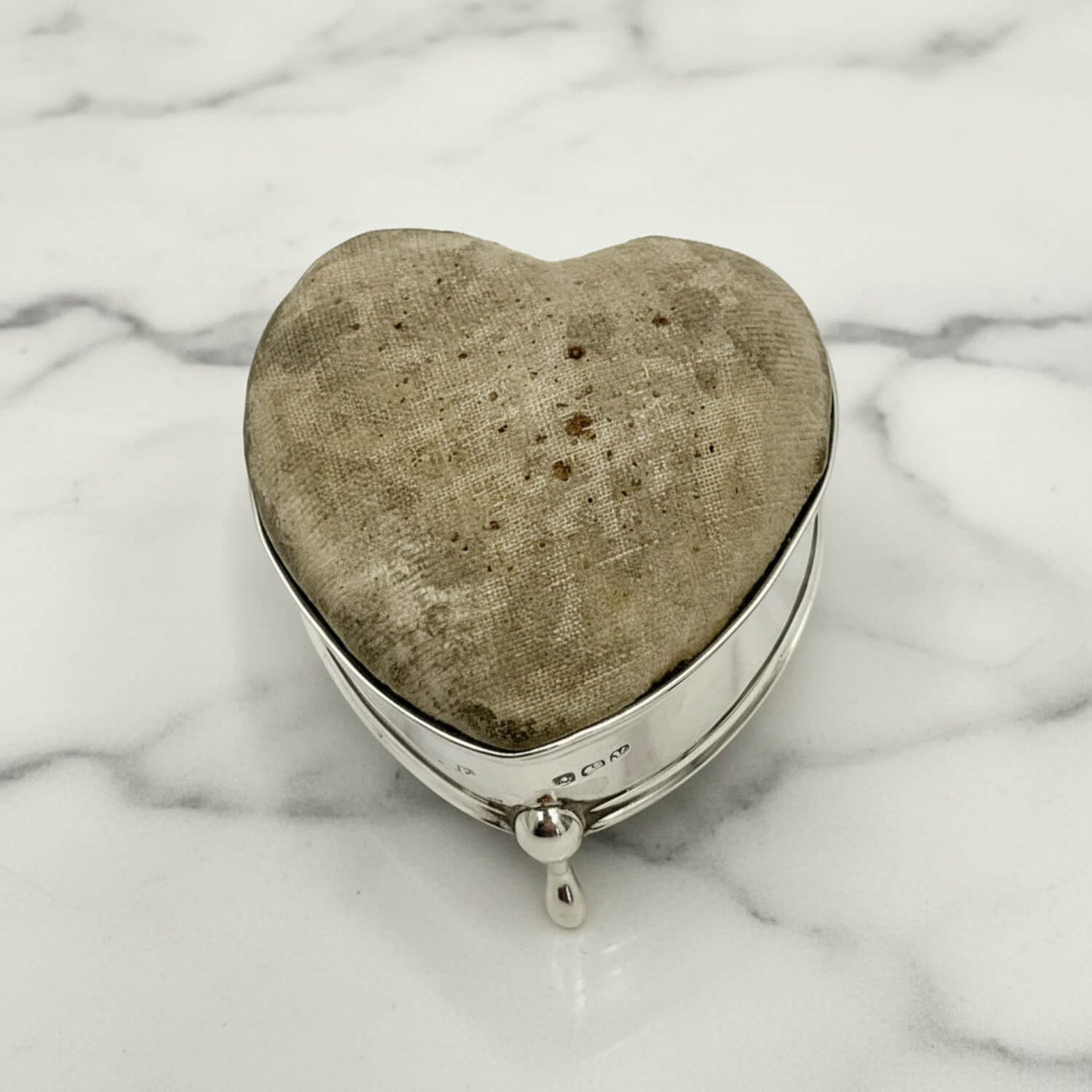 Heart-shaped pincushion with textured fabric interior on a marble surface