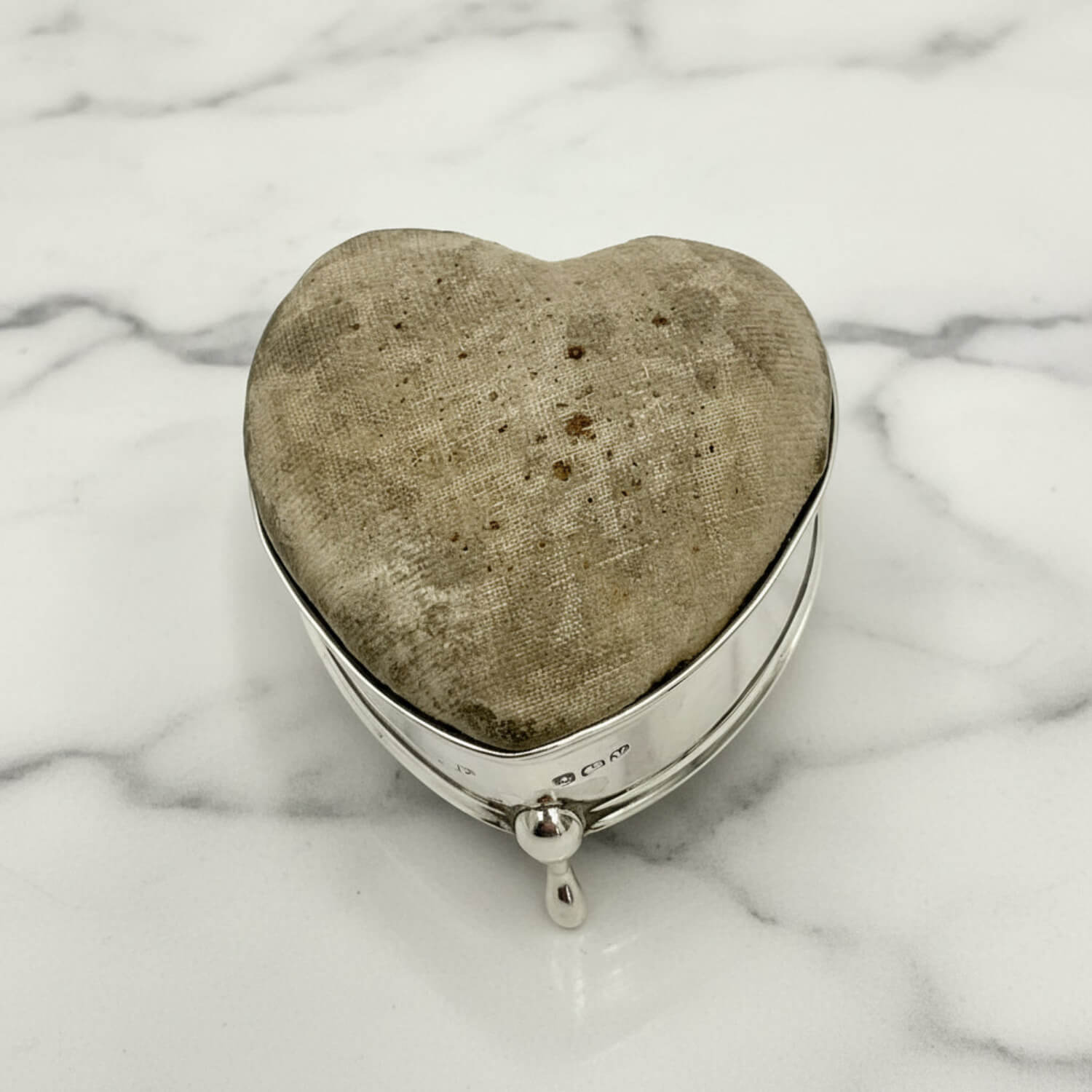 Heart-shaped pincushion with textured fabric interior on a marble surface