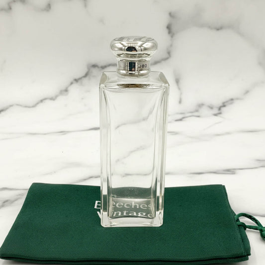 Clear glass perfume bottle with silver cap on a green cloth with 'Beeches Vintage' branding against a marble background.