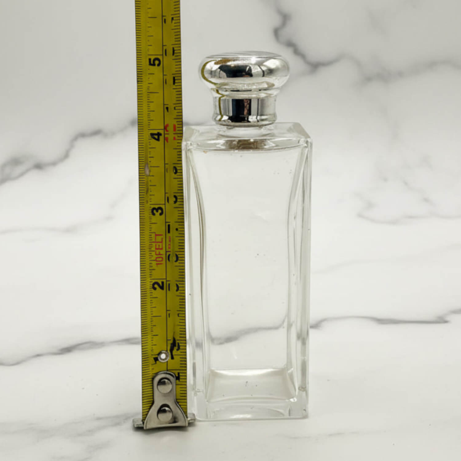 Clear glass bottle with silver cap on a marble surface, measured by a ruler.