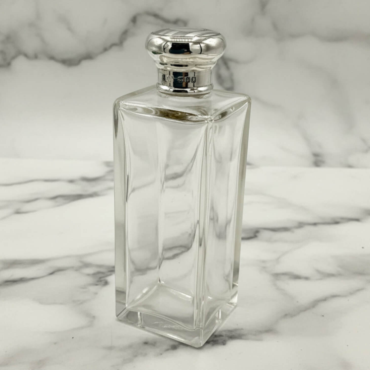Clear glass bottle with silver cap on a marble background