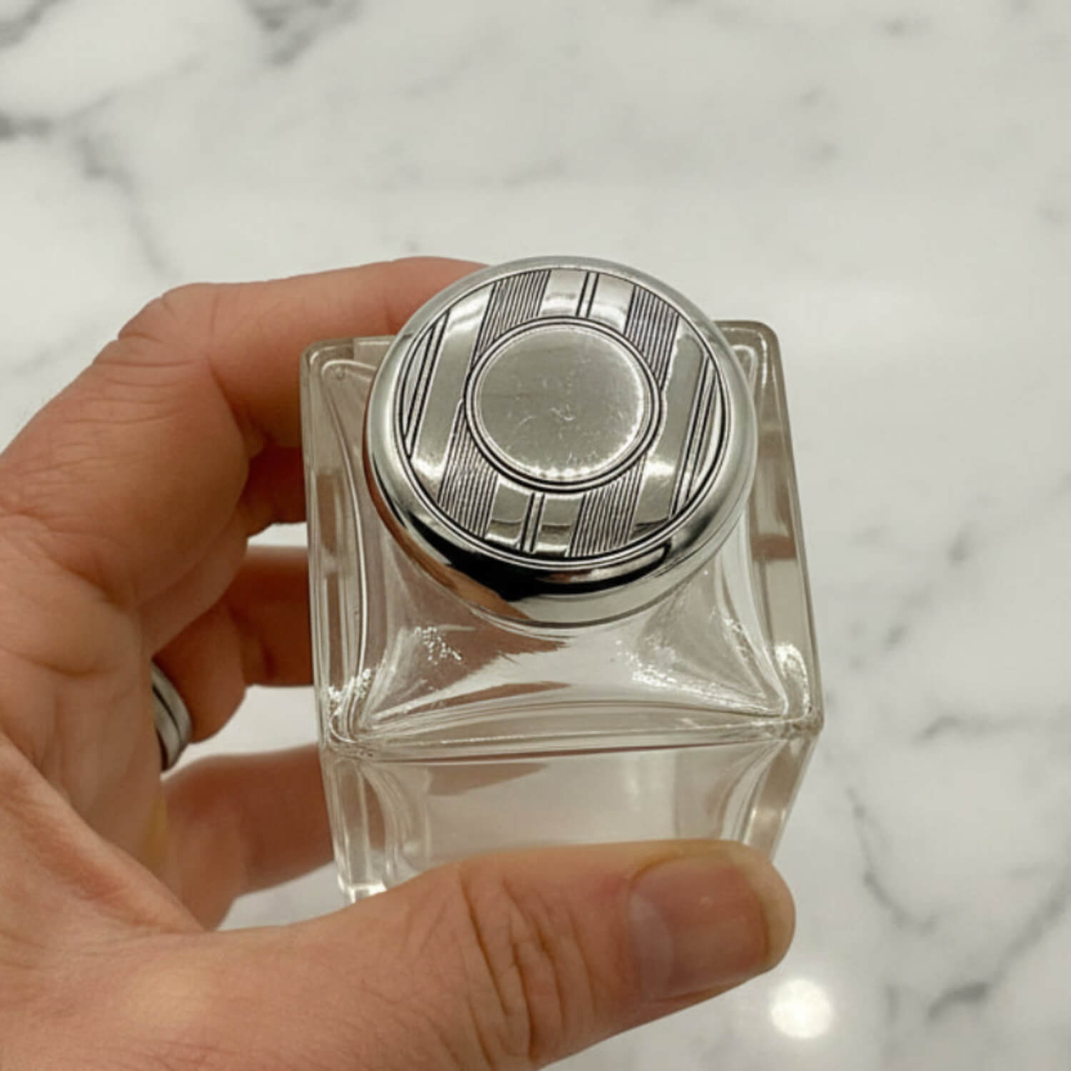 Hand holding a clear glass bottle with a silver cap against a marble background