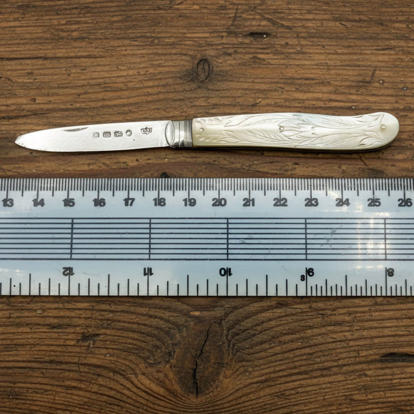 Silver knife with pearl handle on a wooden surface next to a ruler